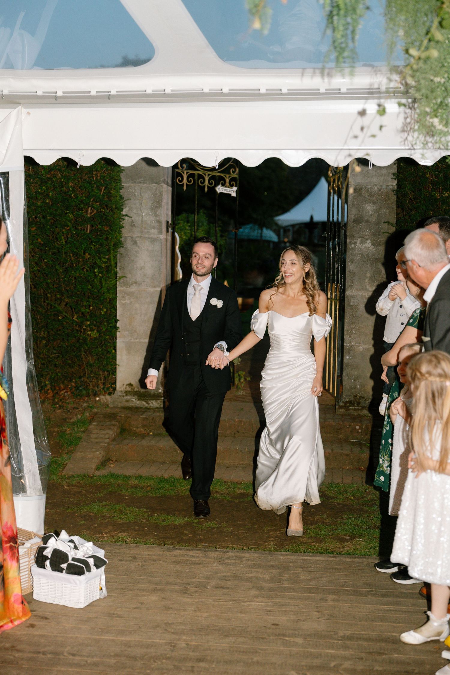 Newlyweds walking through decorated archway during wedding celebration.