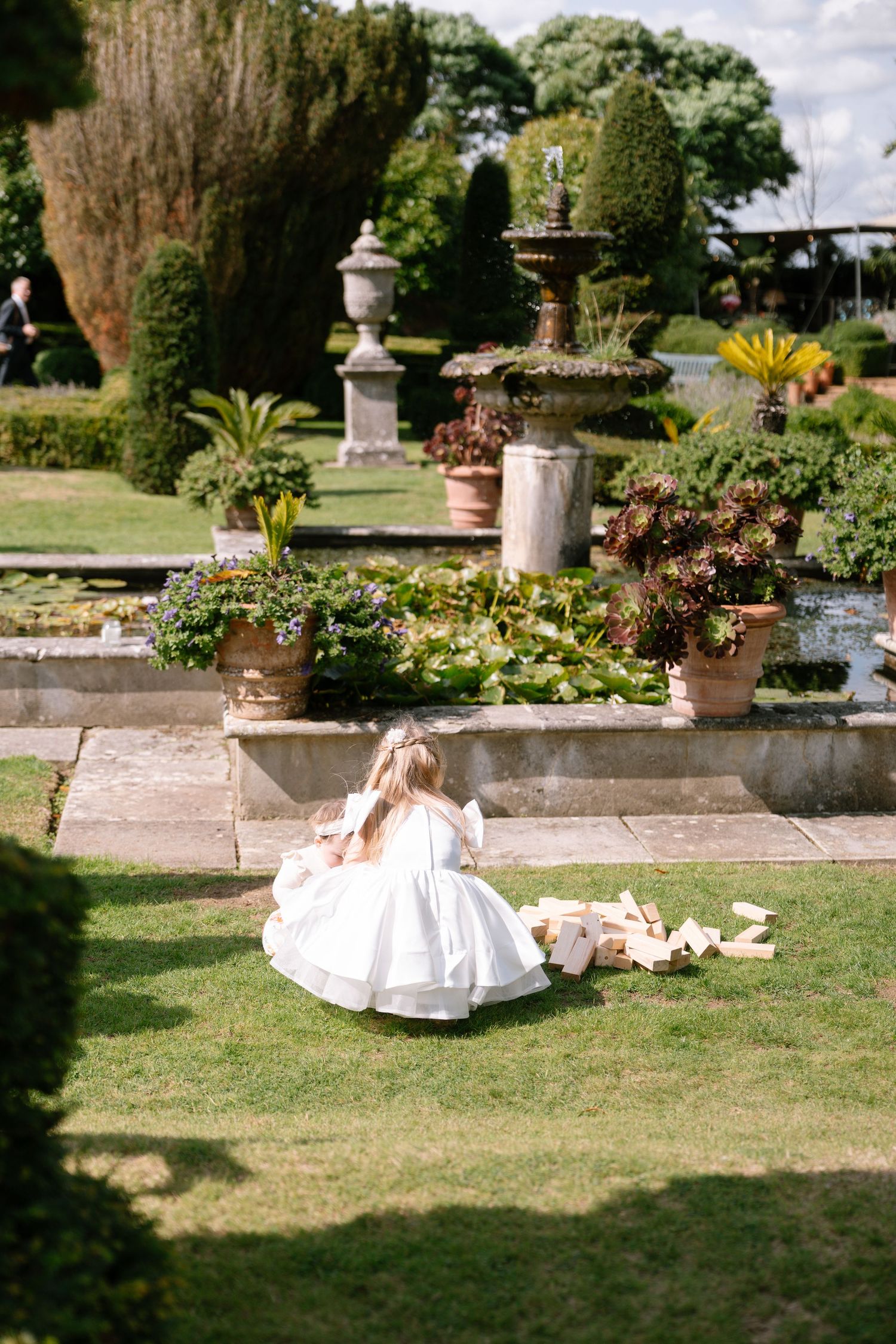 Wedding dress spread out on grass in a formal garden setting.