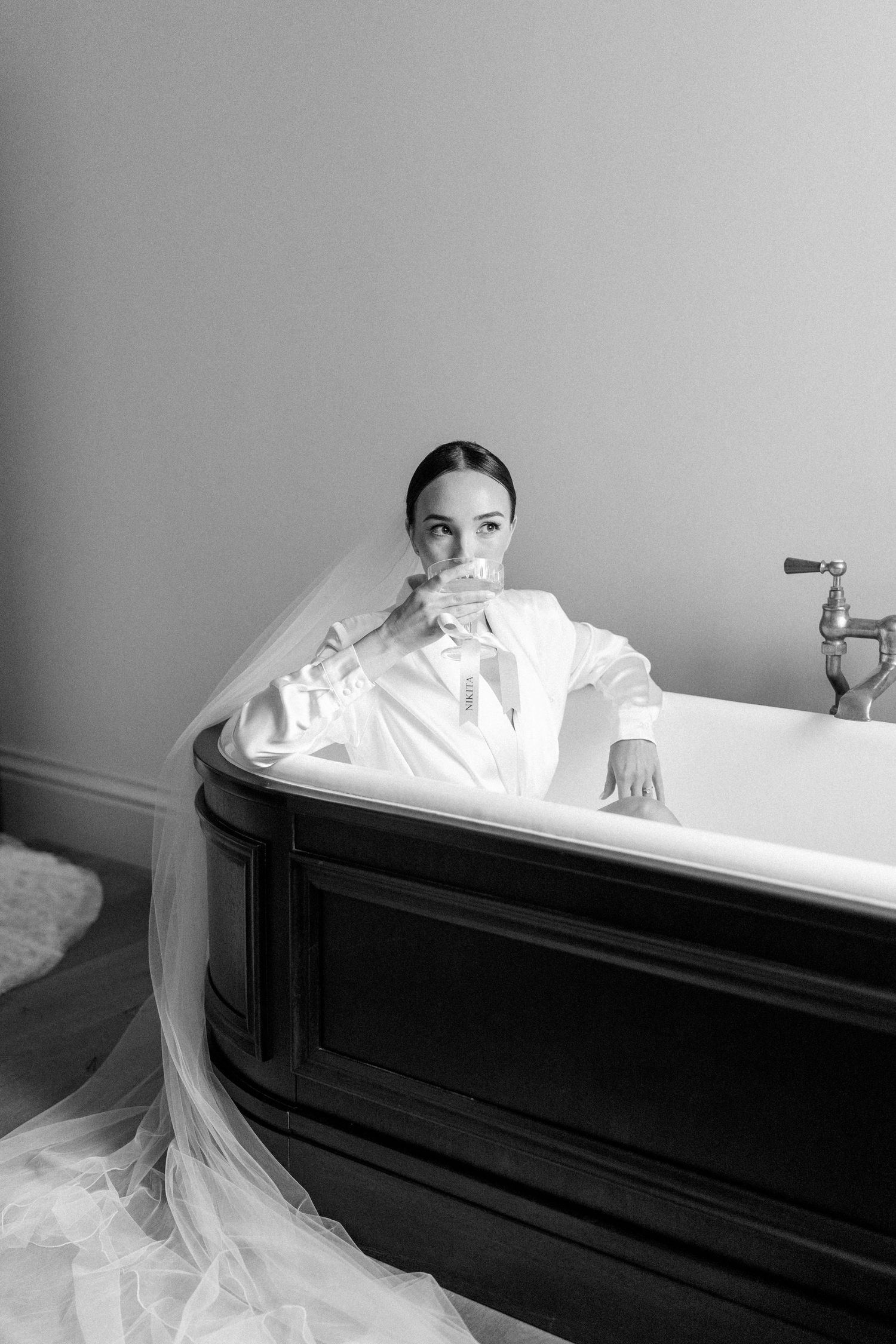 Elegant black and white photo of person in bathtub with flowing white fabric.