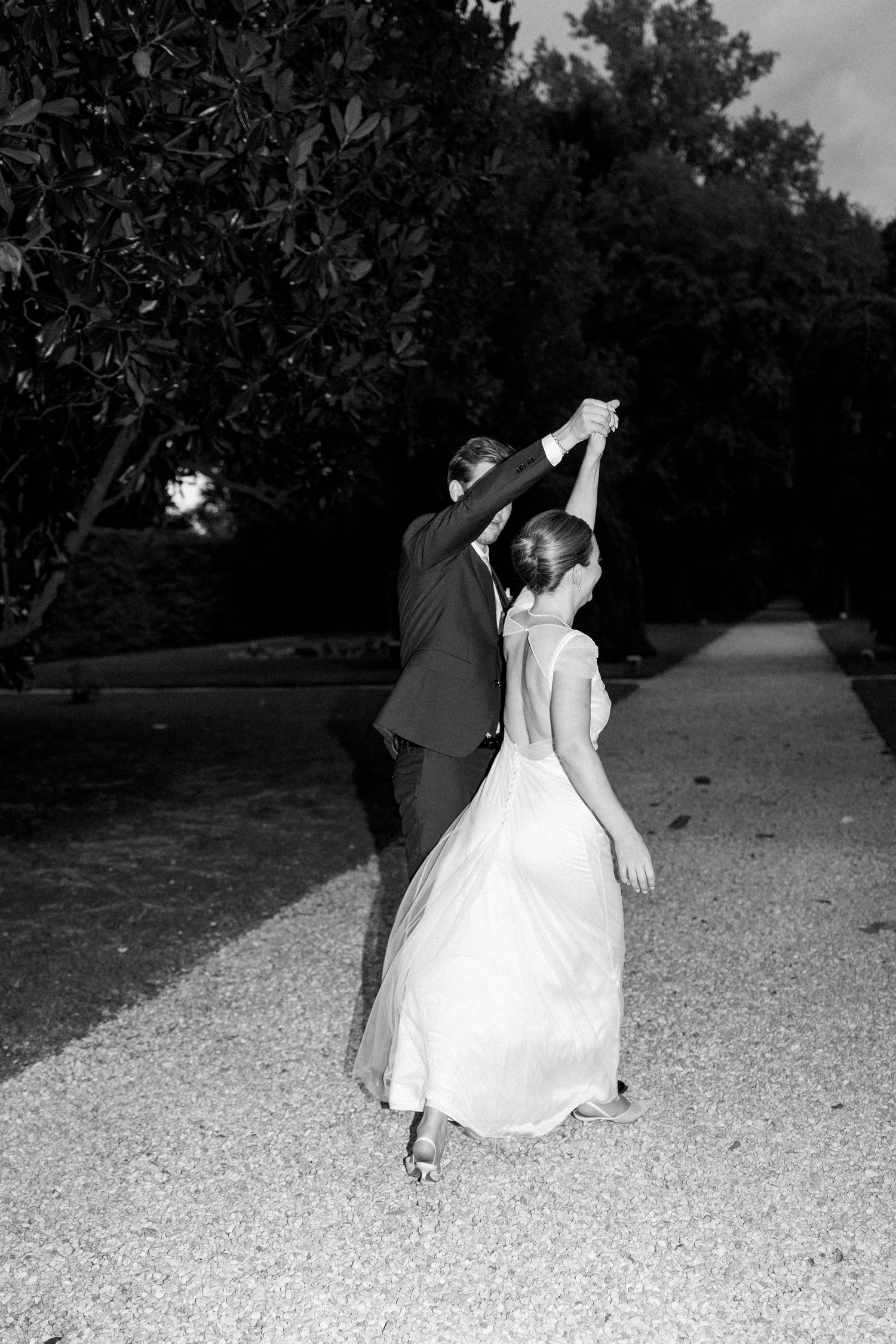 Dancing couple spins on gravel path during evening wedding celebration.