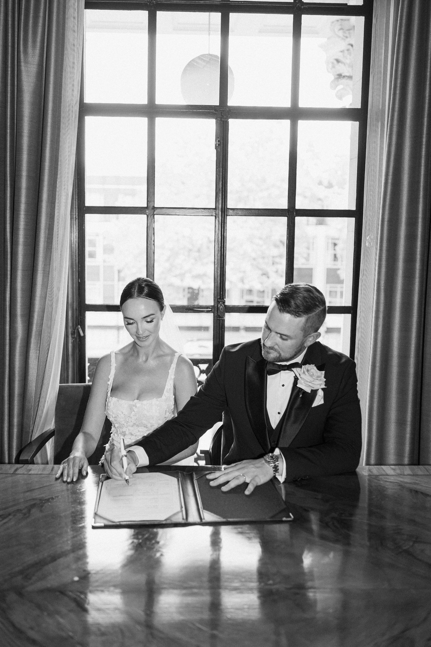 Black and white photo of wedding party members looking down at a wooden table.