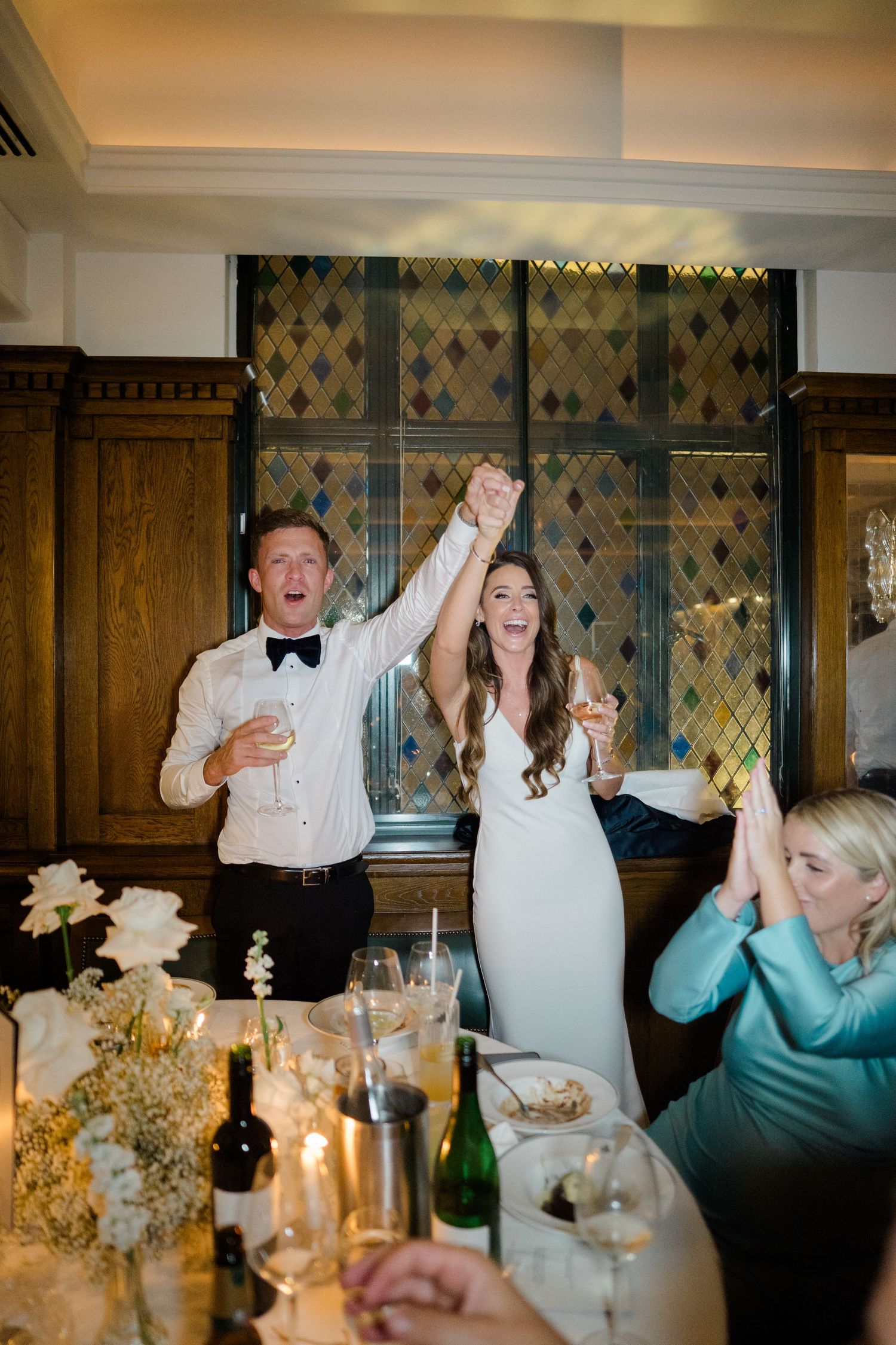 Joyful wedding celebration with guests cheering at reception dinner.