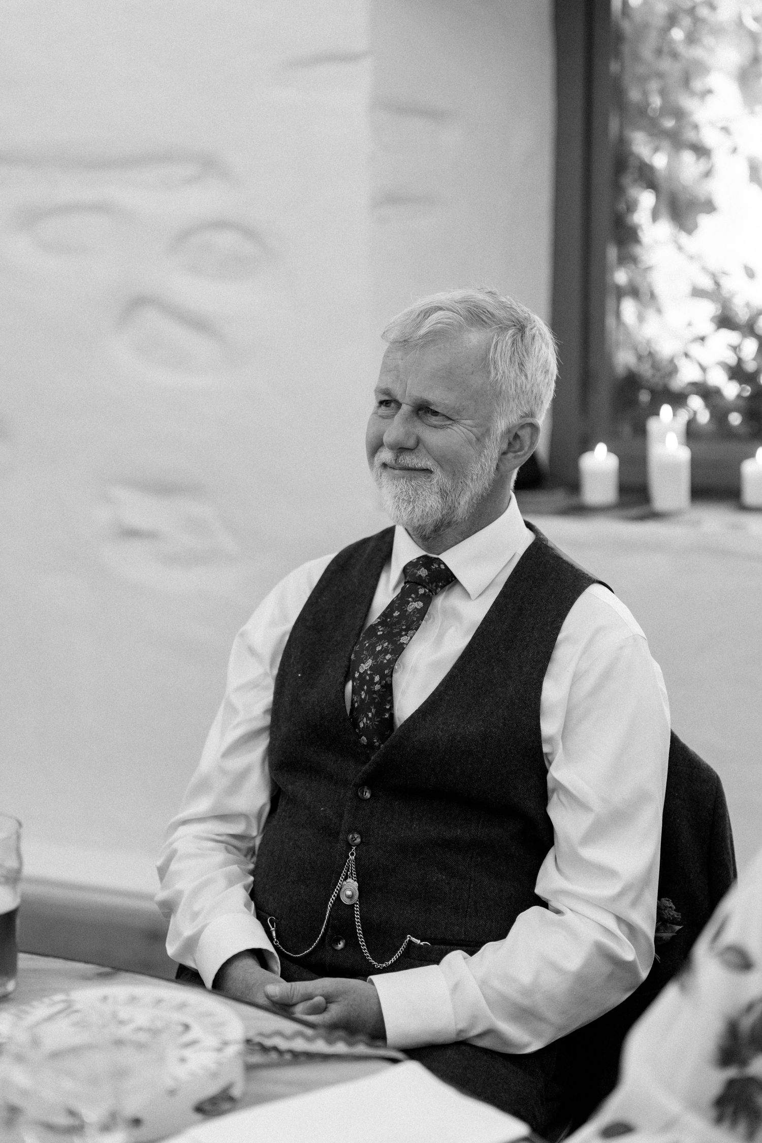 A guest in formal attire sits at a reception table with textured white walls in the background.