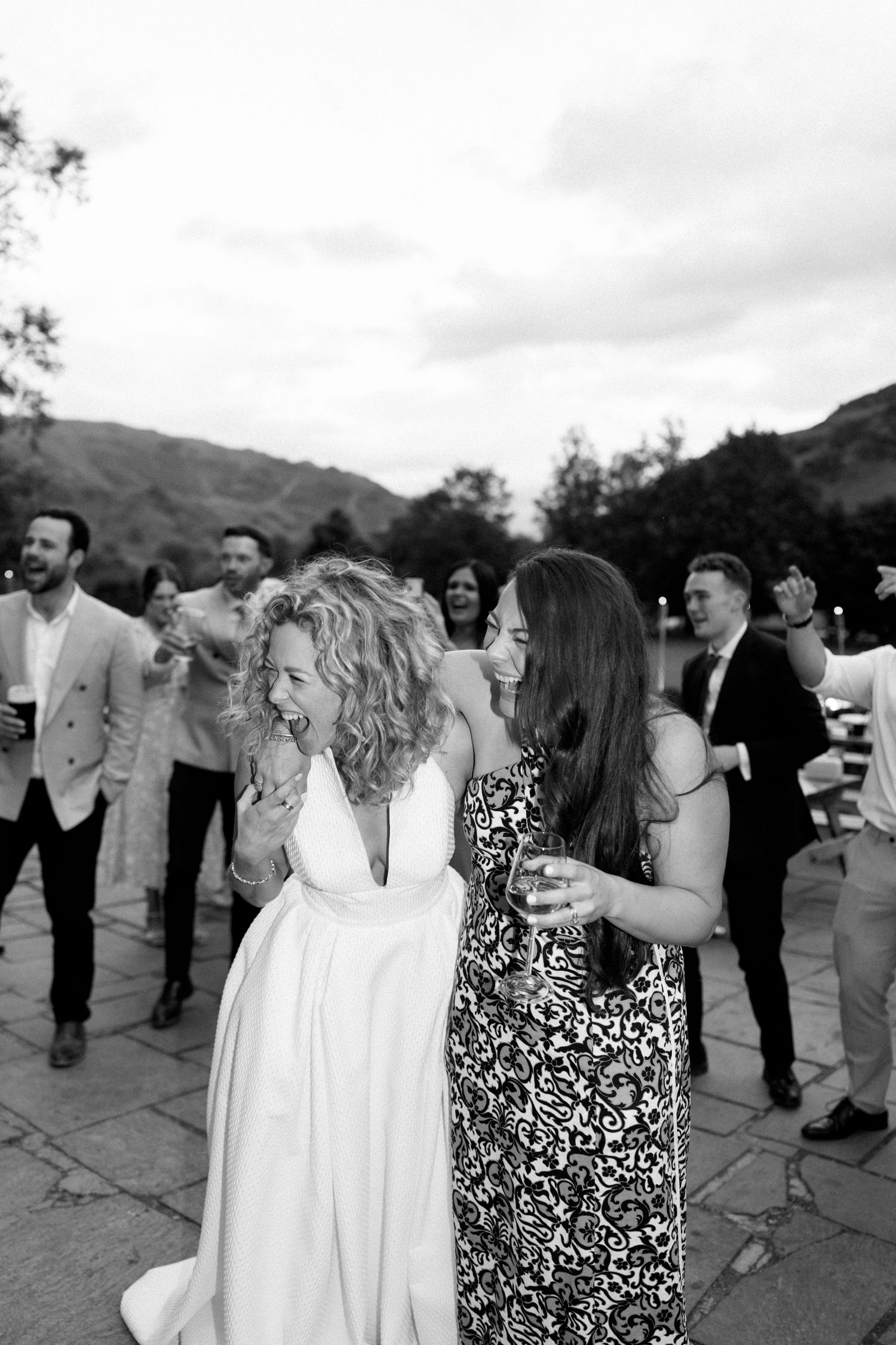Wedding guests gather outdoors for celebration against mountainous backdrop.