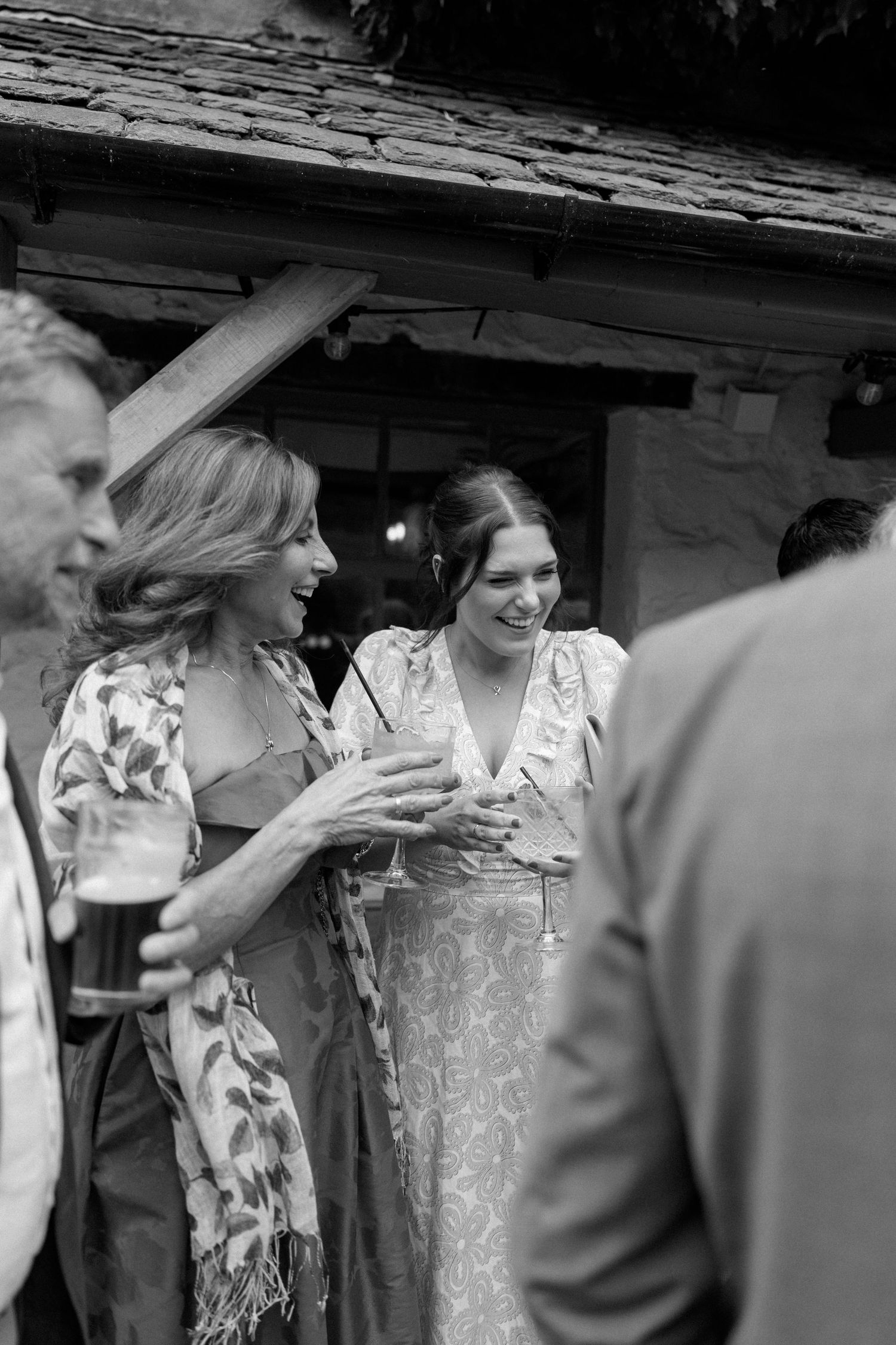 Wedding guests in floral and lace dresses socialize and hold drinks at an outdoor reception.