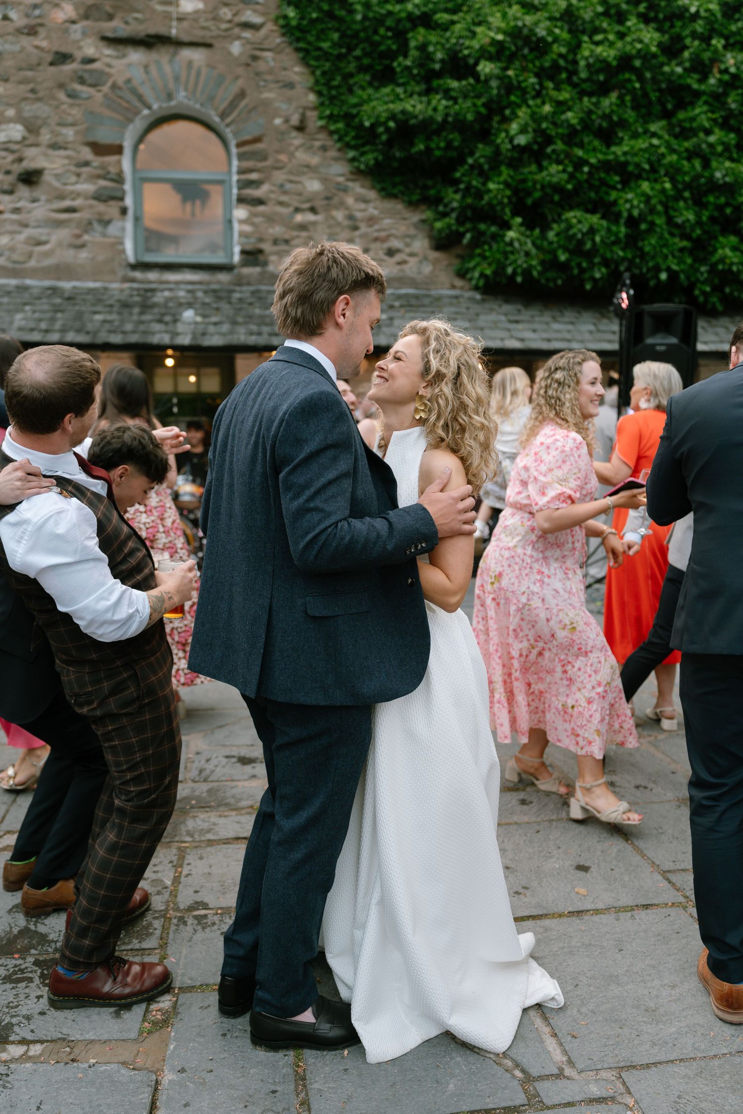 Wedding guests dancing outside a stone building during reception celebrations.