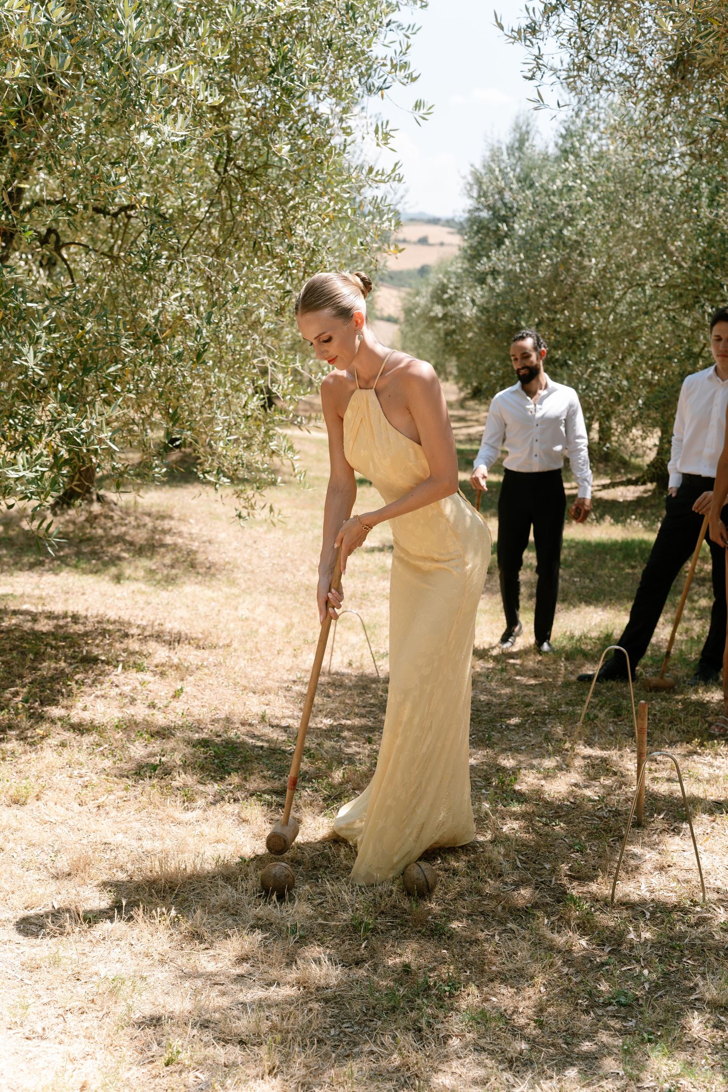 Group playing croquet in an olive grove during a summer gathering.