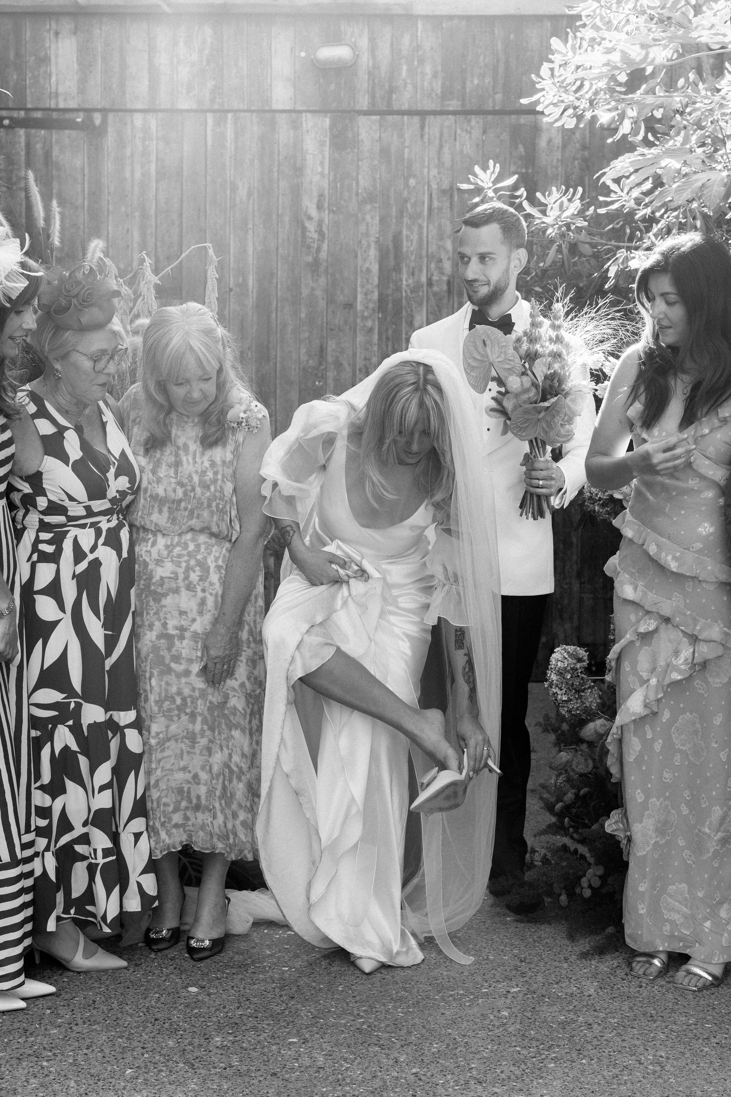 Wedding guests lined up against a fence for a group photo in black and white.