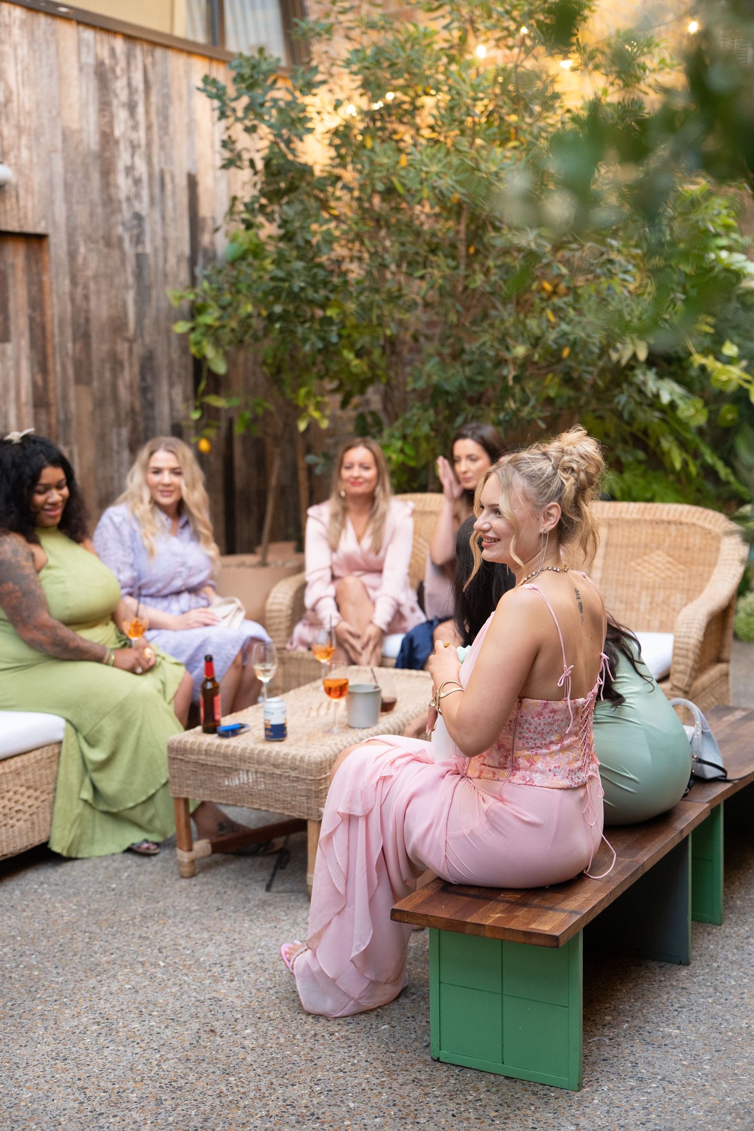 A group of wedding guests in pastel dresses relax on outdoor furniture.