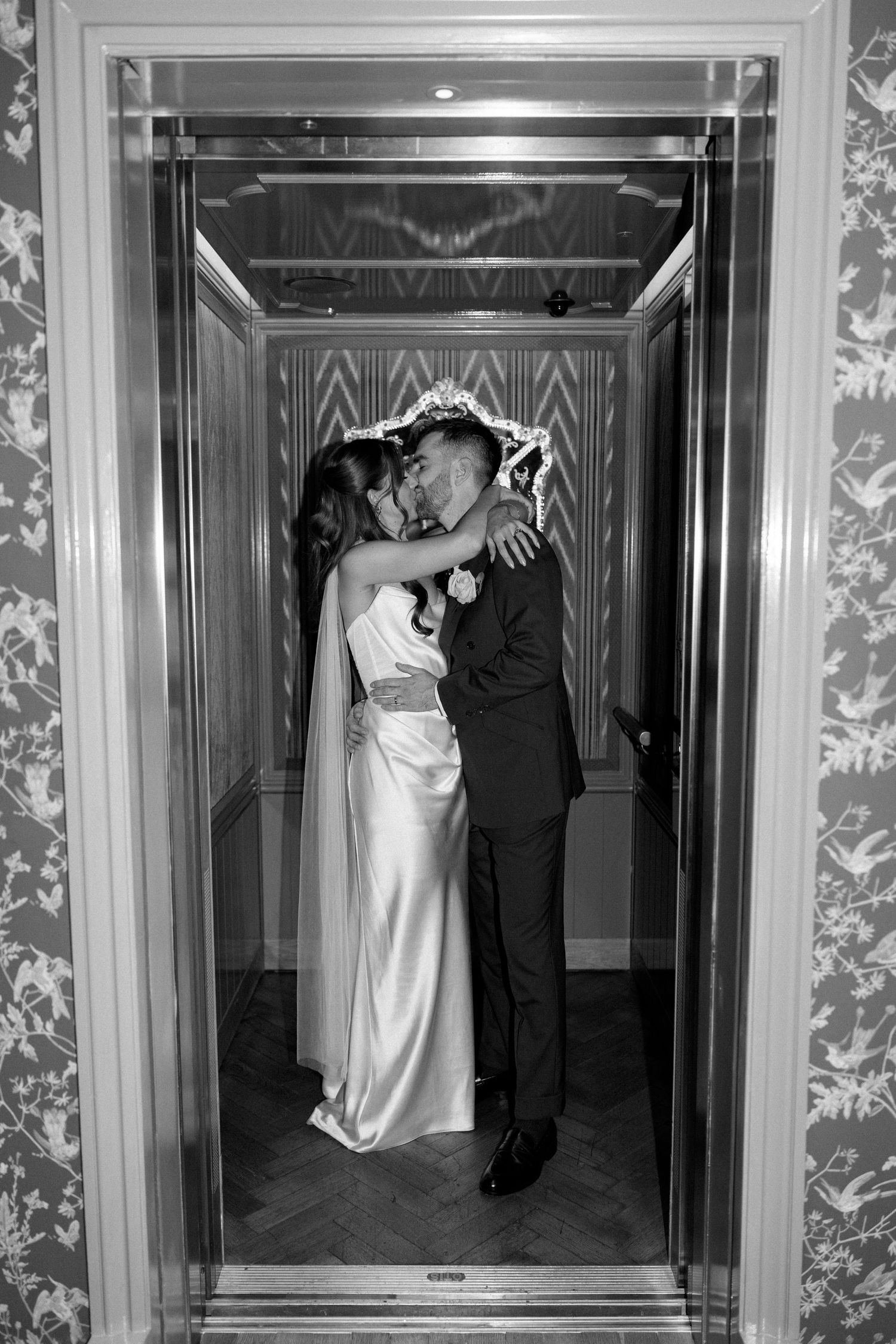 Black and white photo of bride and groom kissing in elevator on wedding day.