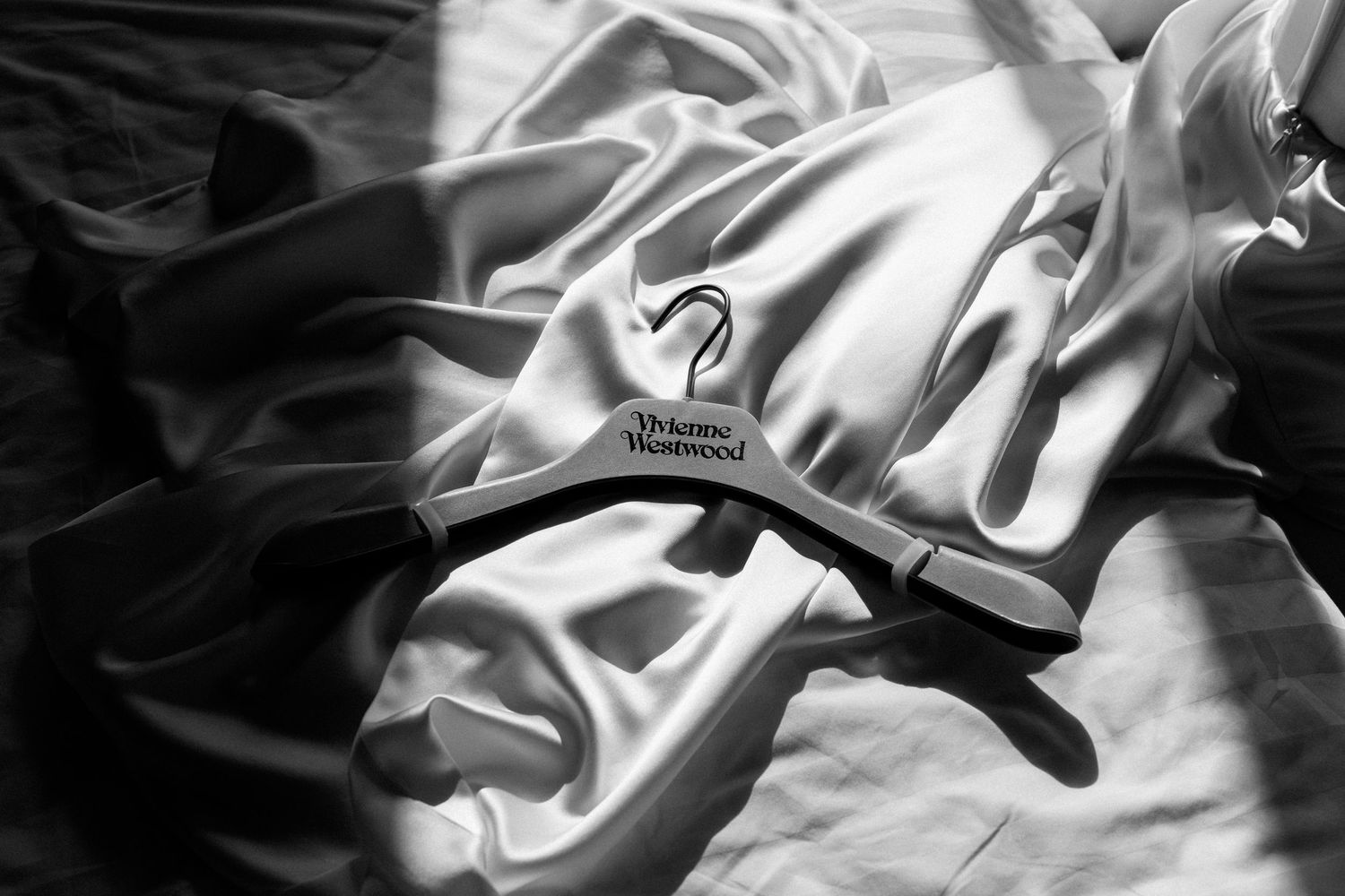 Black and white photo of a Vivienne Westwood branded wooden hanger resting on white satin fabric.