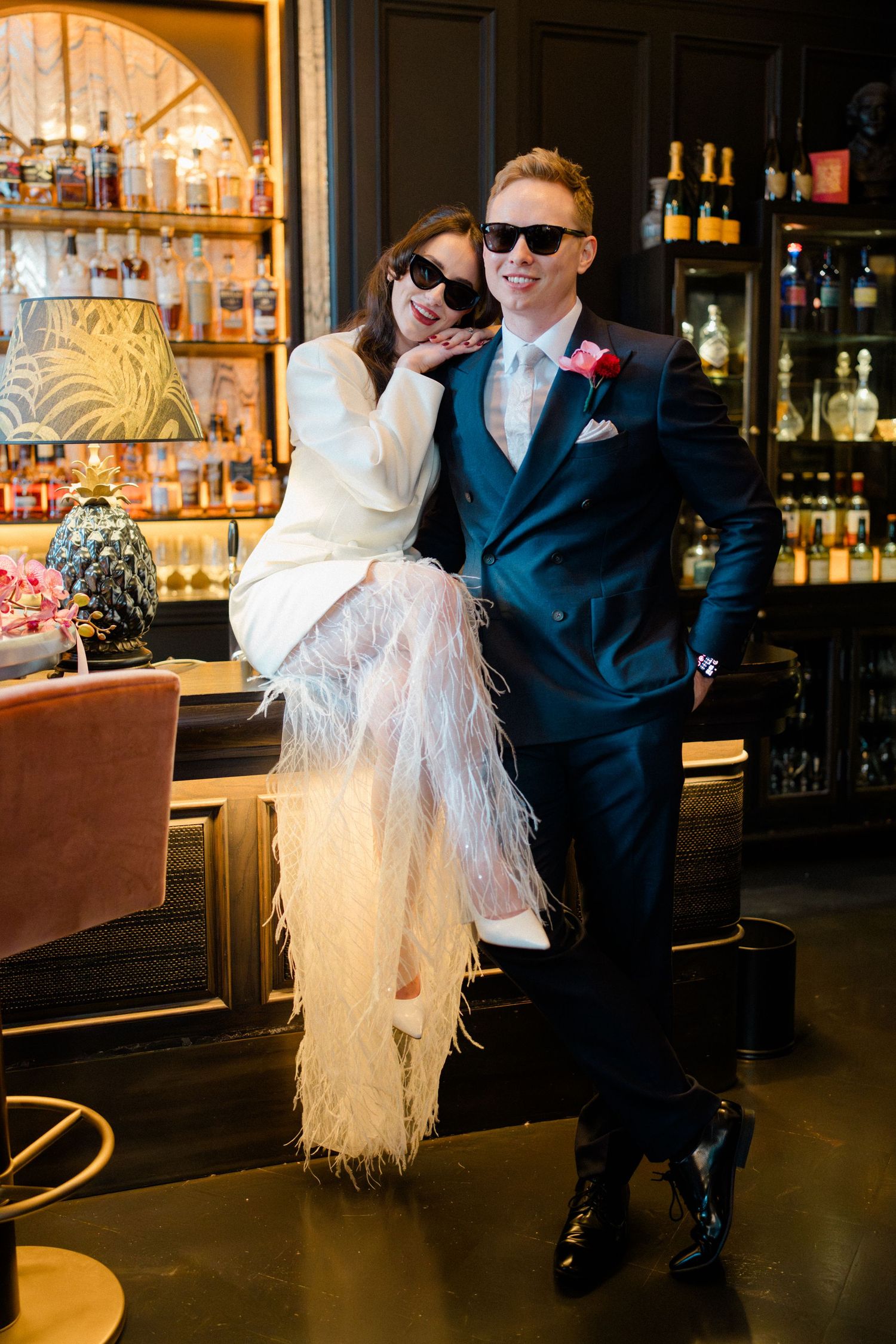Stylish bride and groom in sunglasses posing together in a sophisticated hotel bar.