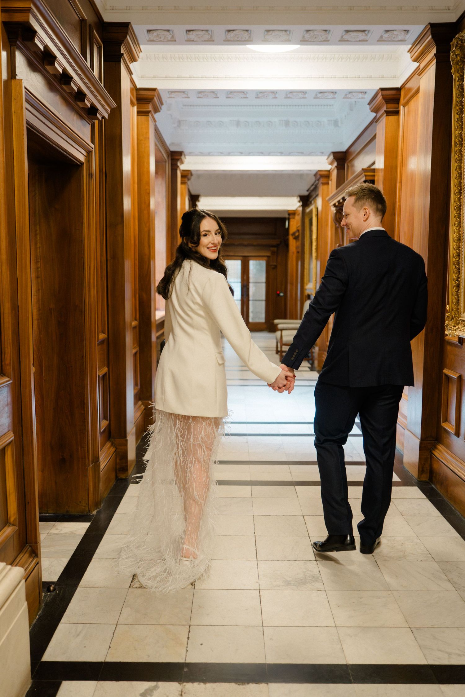 Bride and groom holding hands walking through an elegant wood-paneled hallway after their ceremony.