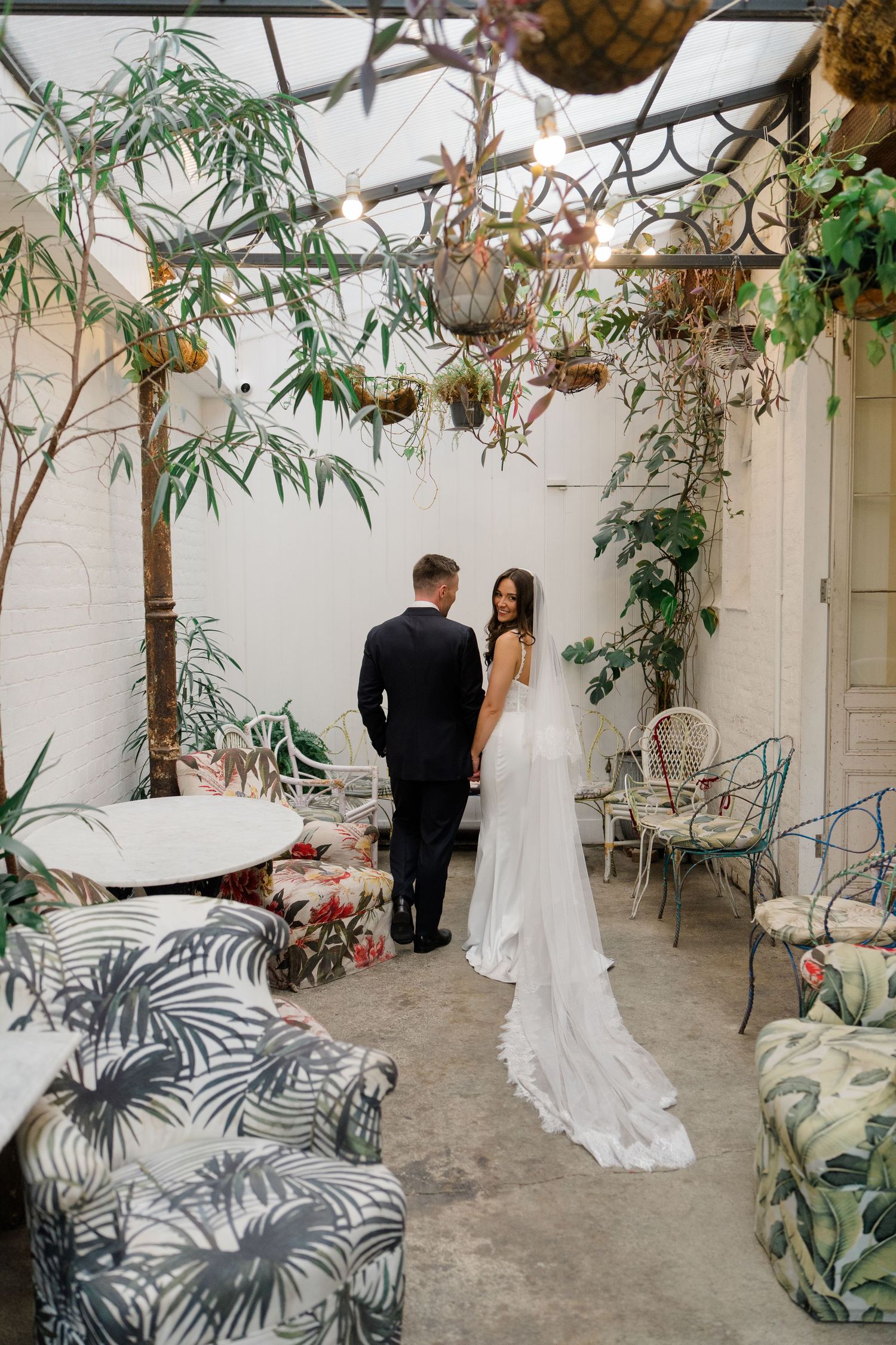Bride and groom holding hands in a lush botanical garden wedding venue with tropical decor.