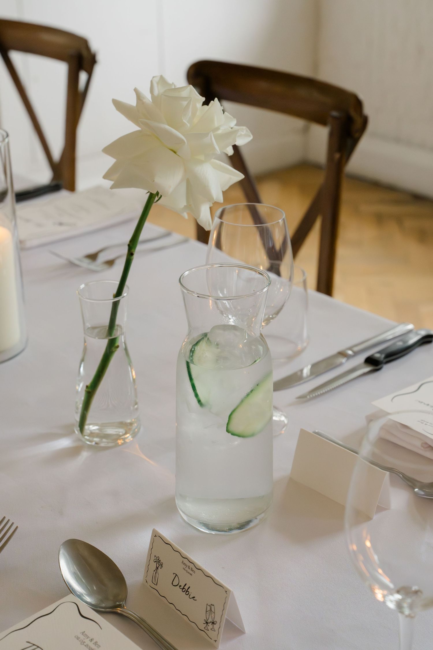 Minimalist wedding table setting with single white flower in bud vase and cucumber water carafe.