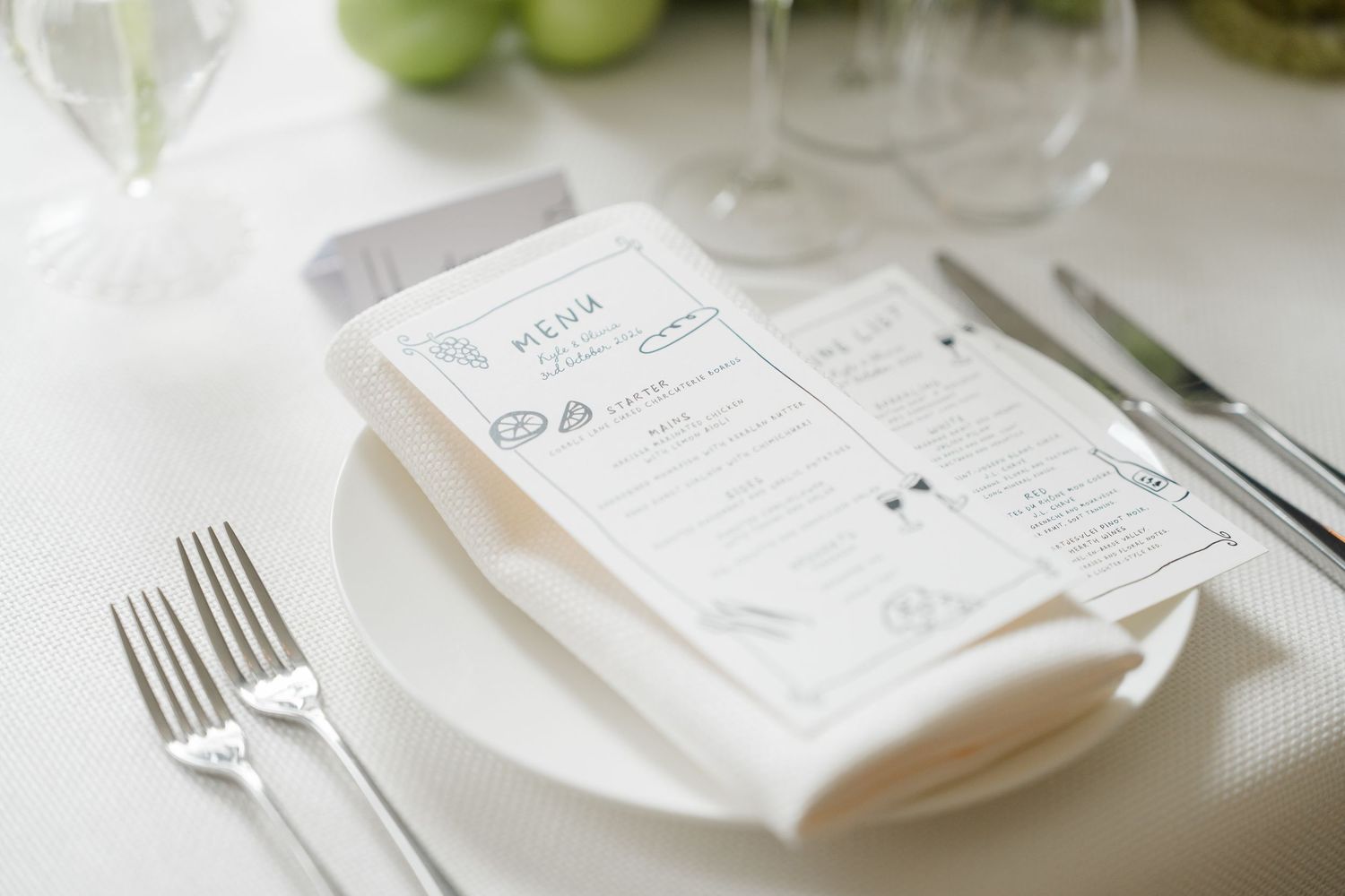 Elegant wedding place setting with folded menu card on white plate with silver cutlery on linen.