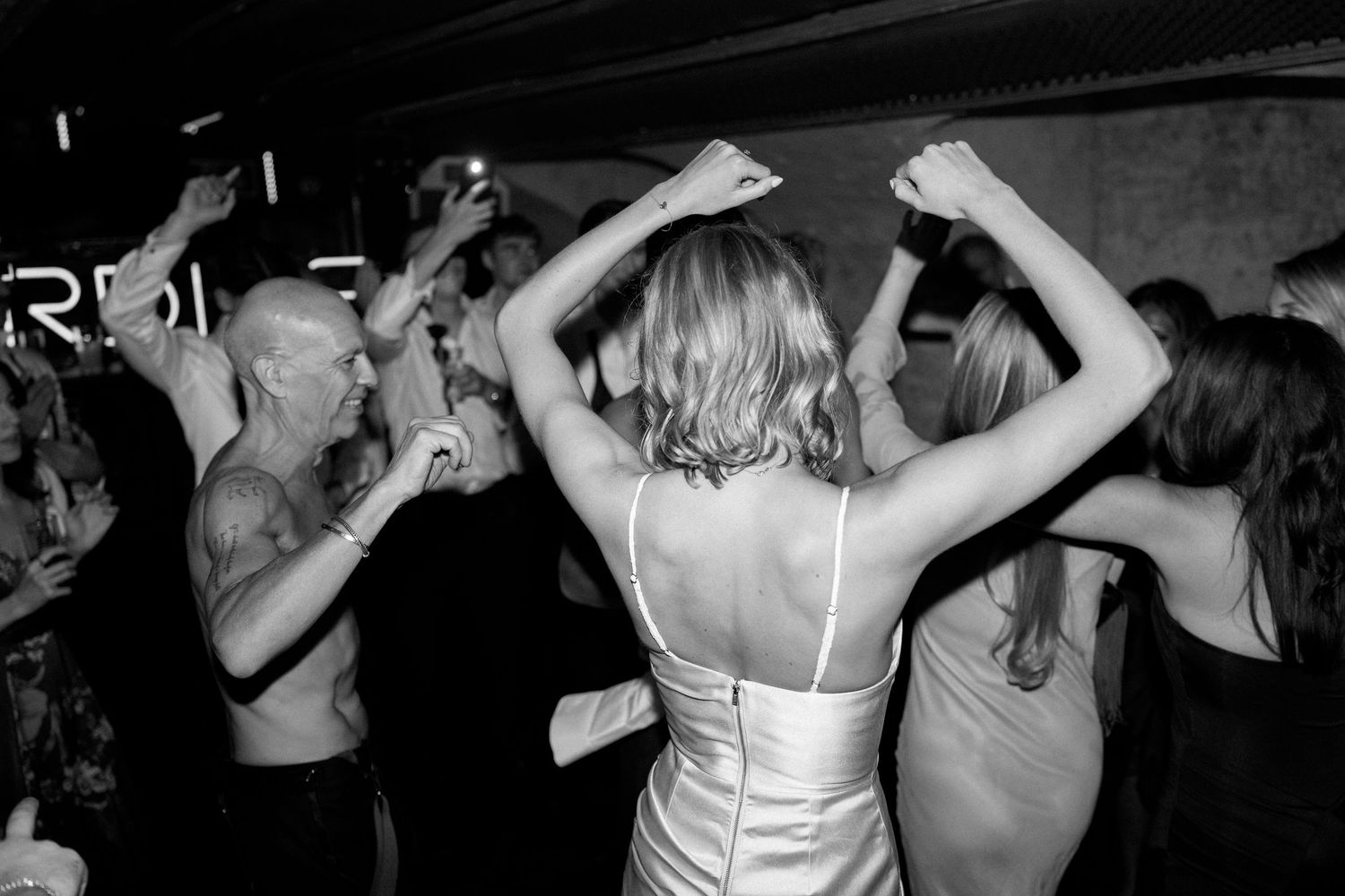 Black and white photo of bride dancing with guests at a lively wedding reception party.