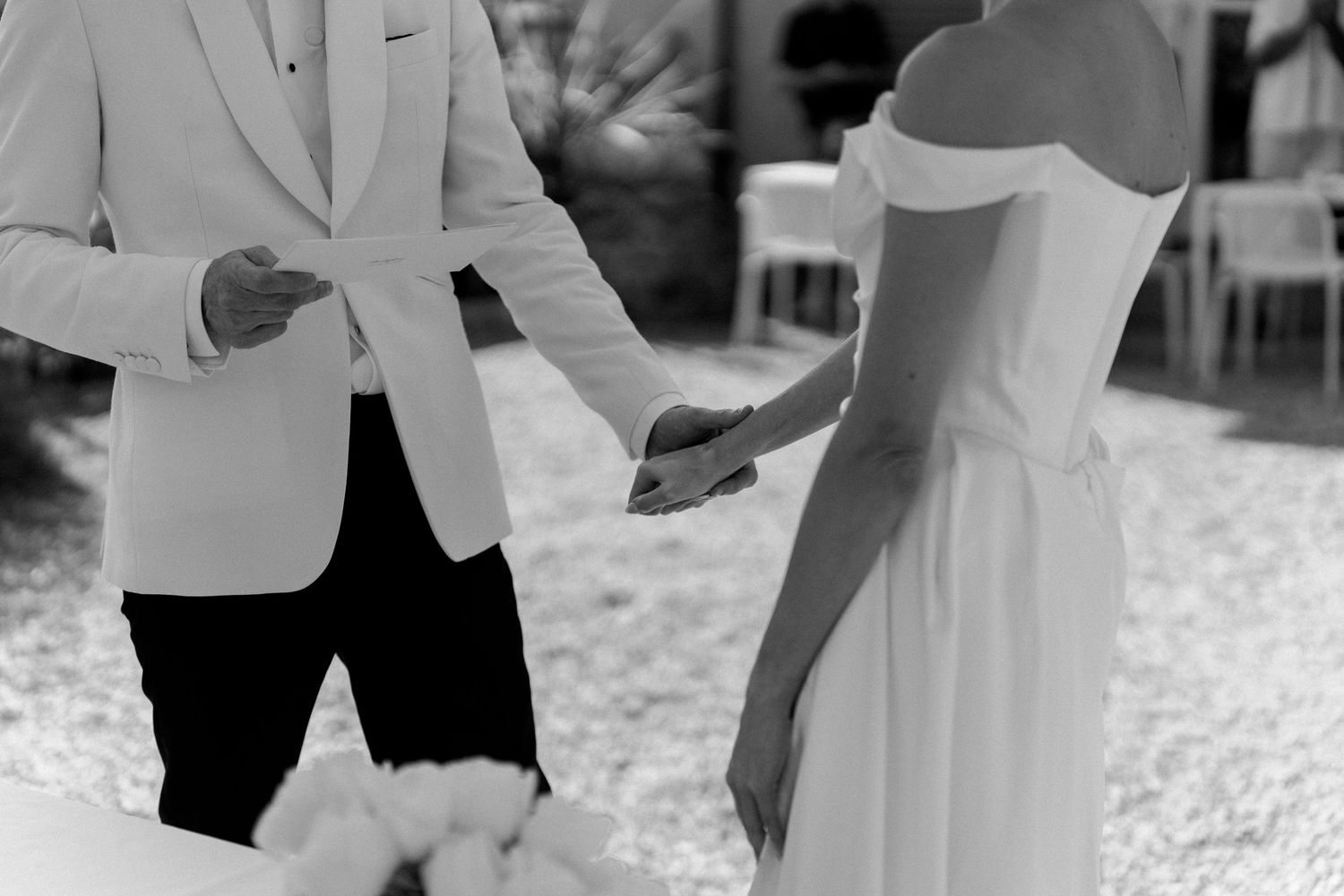 Bride and groom hold hands in black and white wedding photo outdoors.