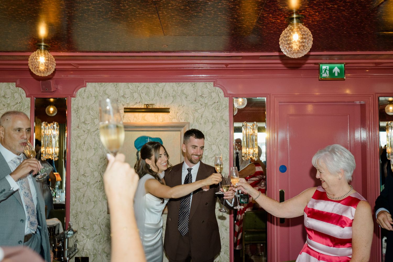 Bride and groom sharing champagne toast with guests in a vibrant pink wedding reception venue.