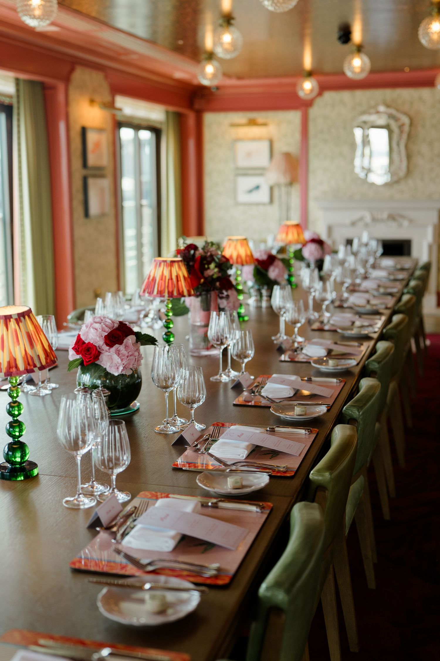 Beautifully set long dining table with crystal glasses, floral centerpieces, and warm lamp lighting.