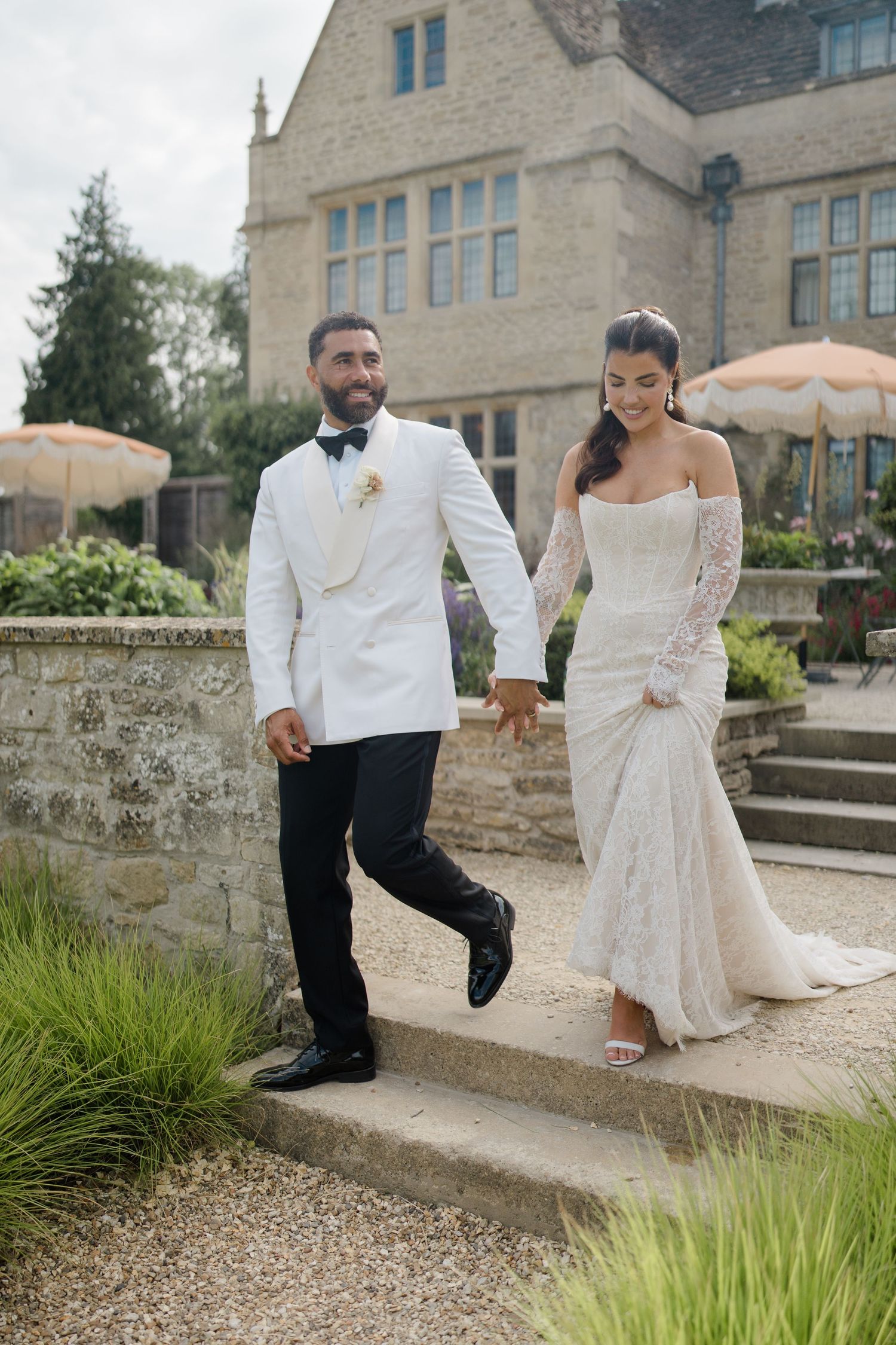 Bride and groom walking hand in hand down stone steps outside a beautiful English manor house wedding venue.
