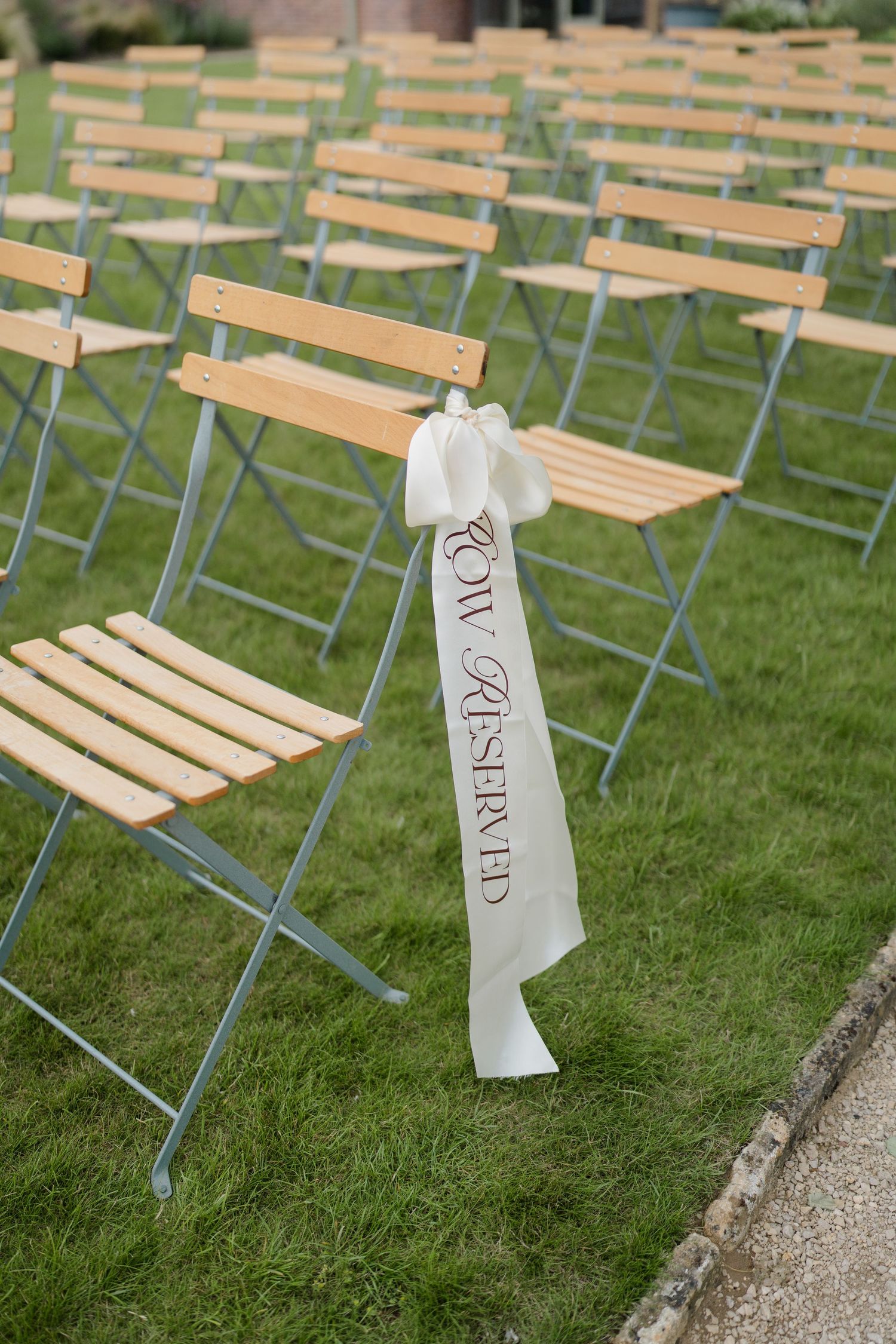 Reserved front row chairs with white ribbon at an elegant outdoor wedding ceremony on green grass.