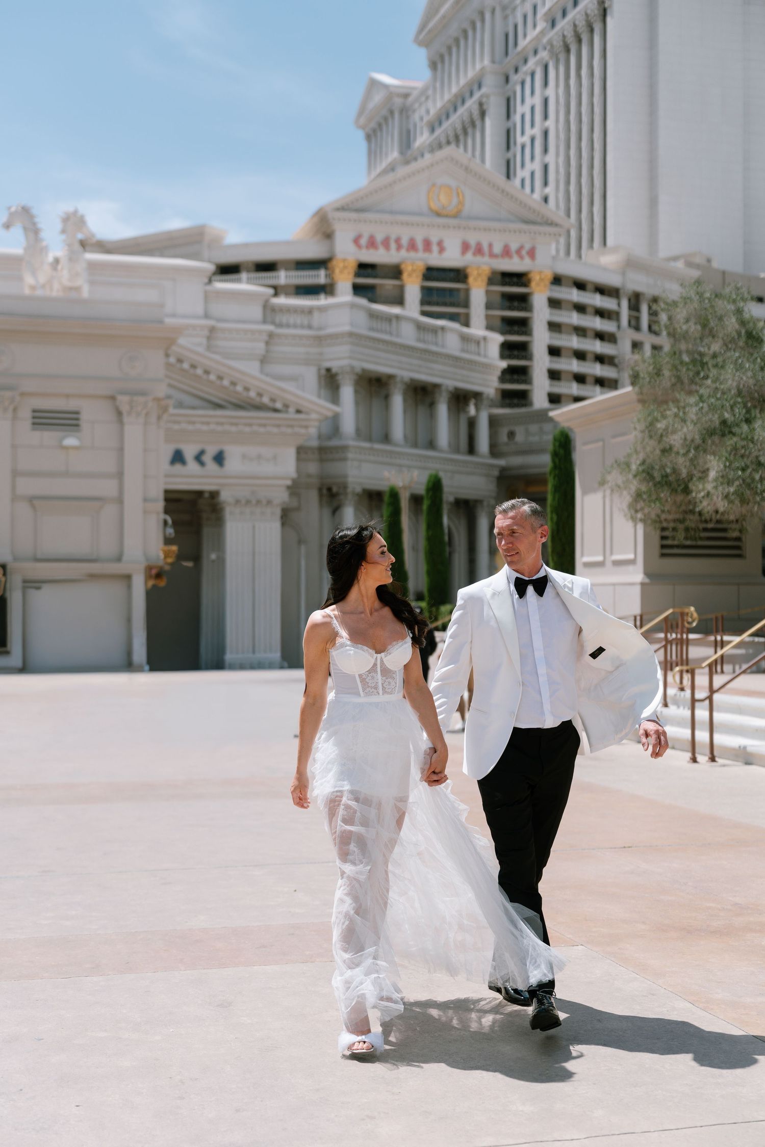 Wedding couple walks along the classical Roman architecture of Caesars Palace Las Vegas.