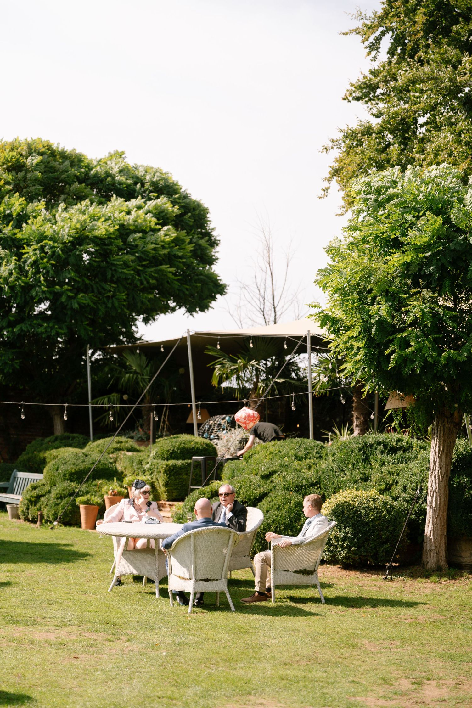 Outdoor wedding lounge area with white furniture and tent setup on green lawn.