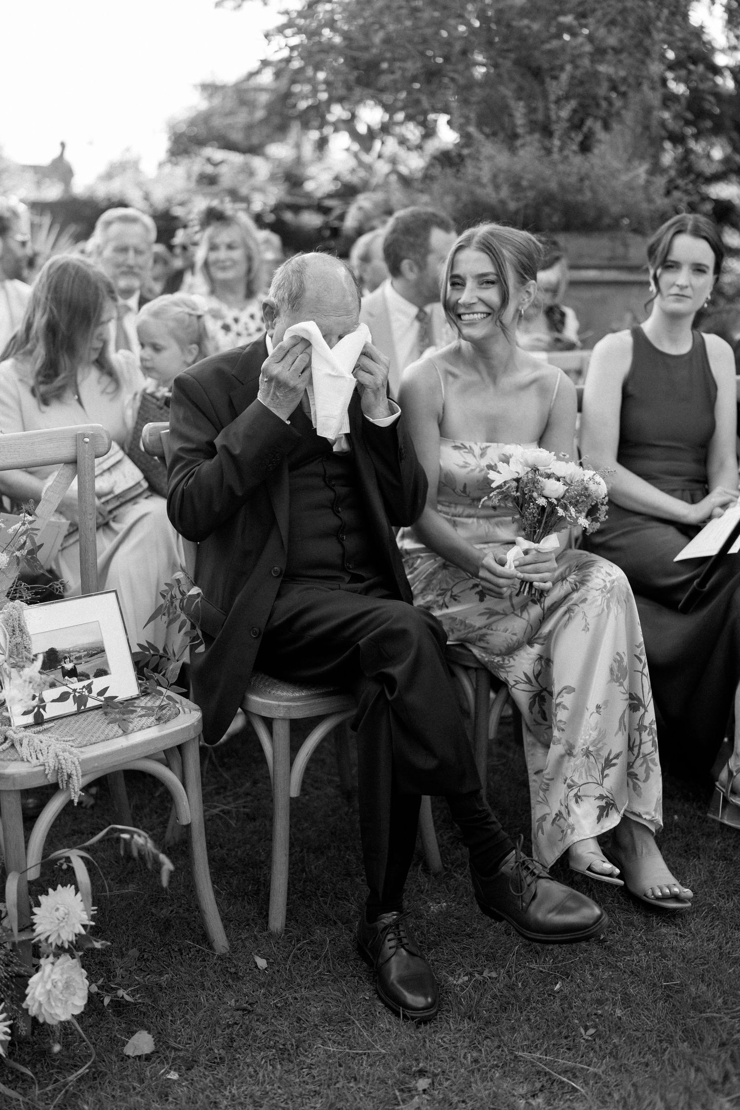 Wedding guests seated in chairs on a lawn share emotional moments during an outdoor ceremony.