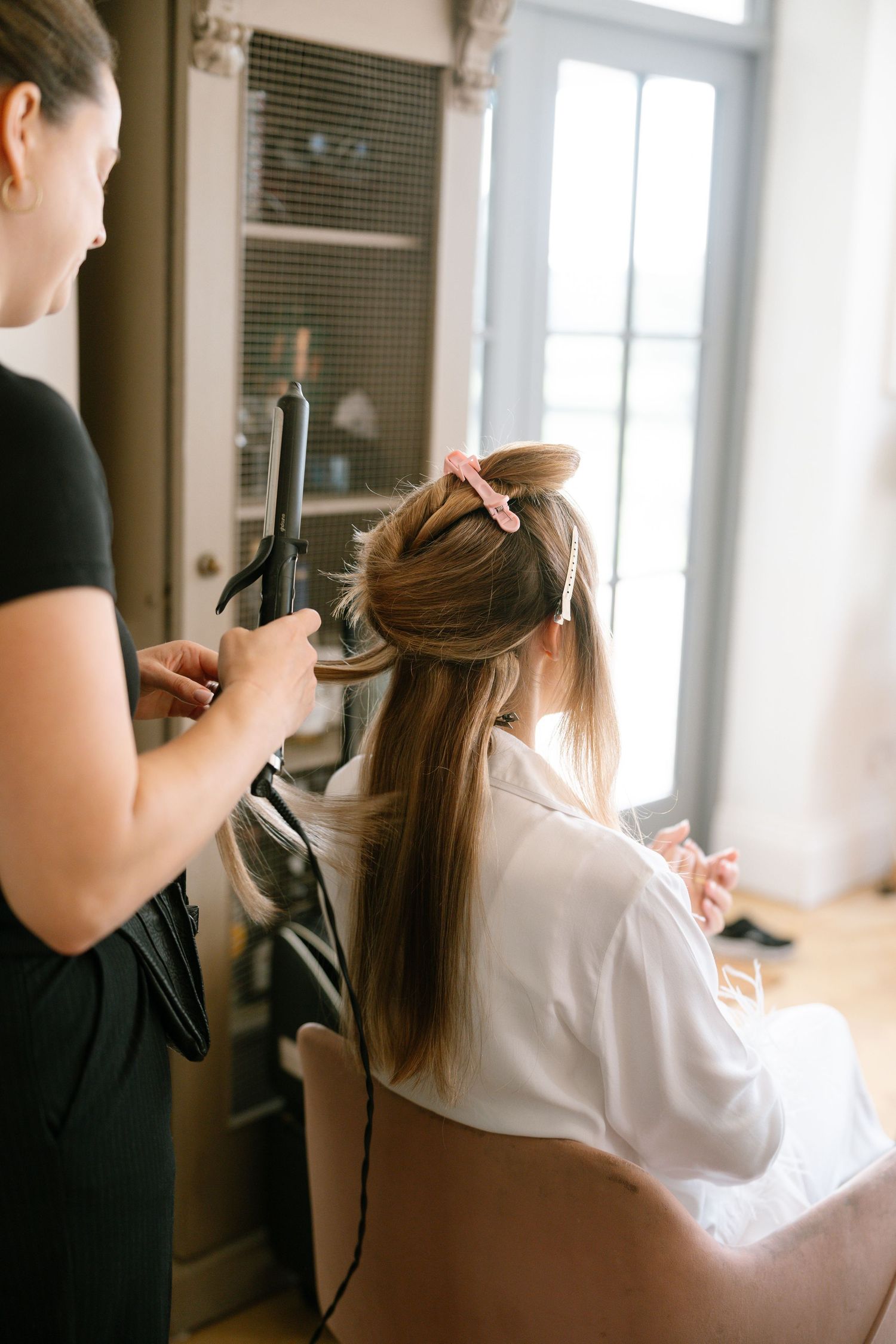 Hair stylist working on client's hair with professional tools in natural light setting.