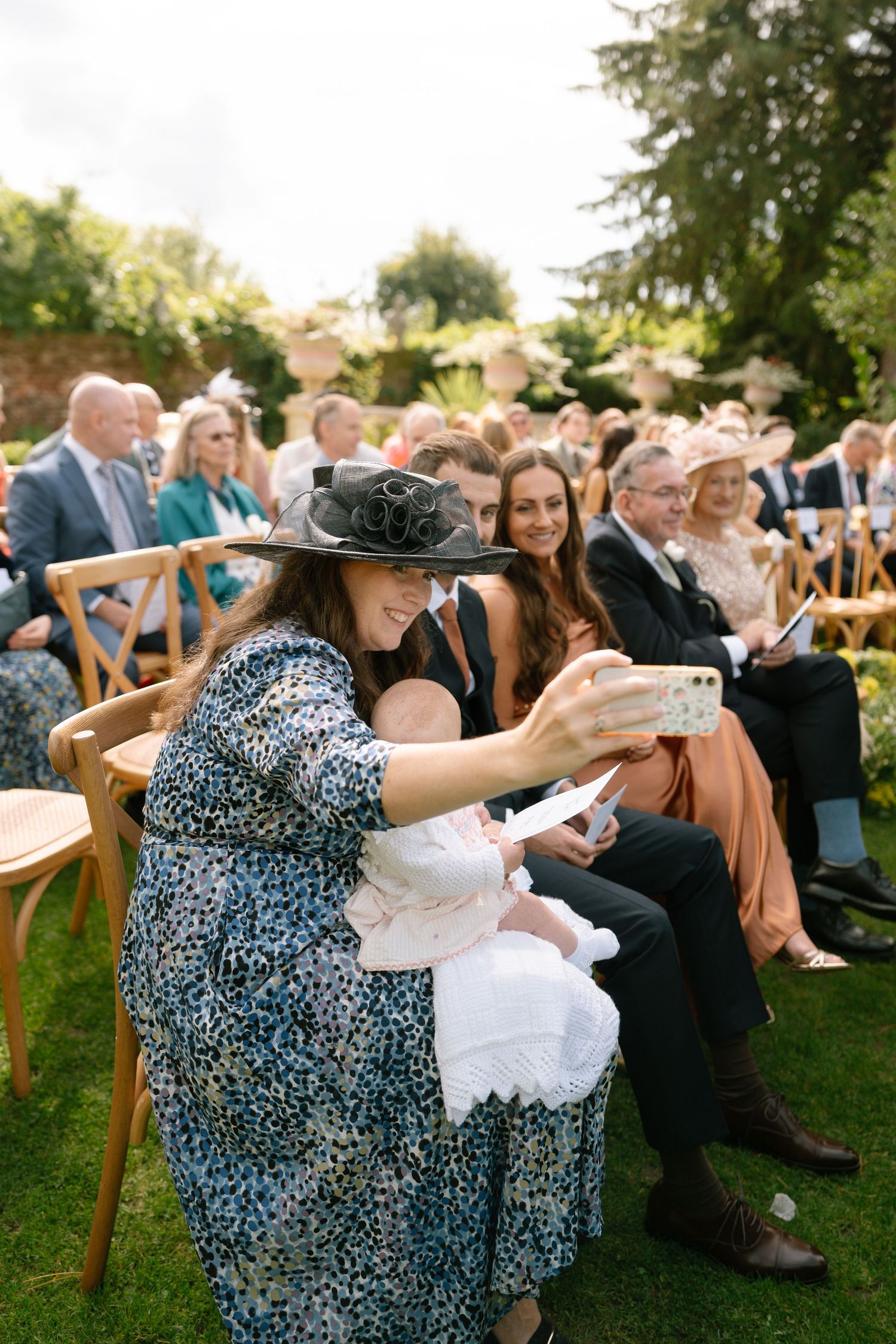 Wedding guests seated in wooden chairs during an outdoor garden ceremony.