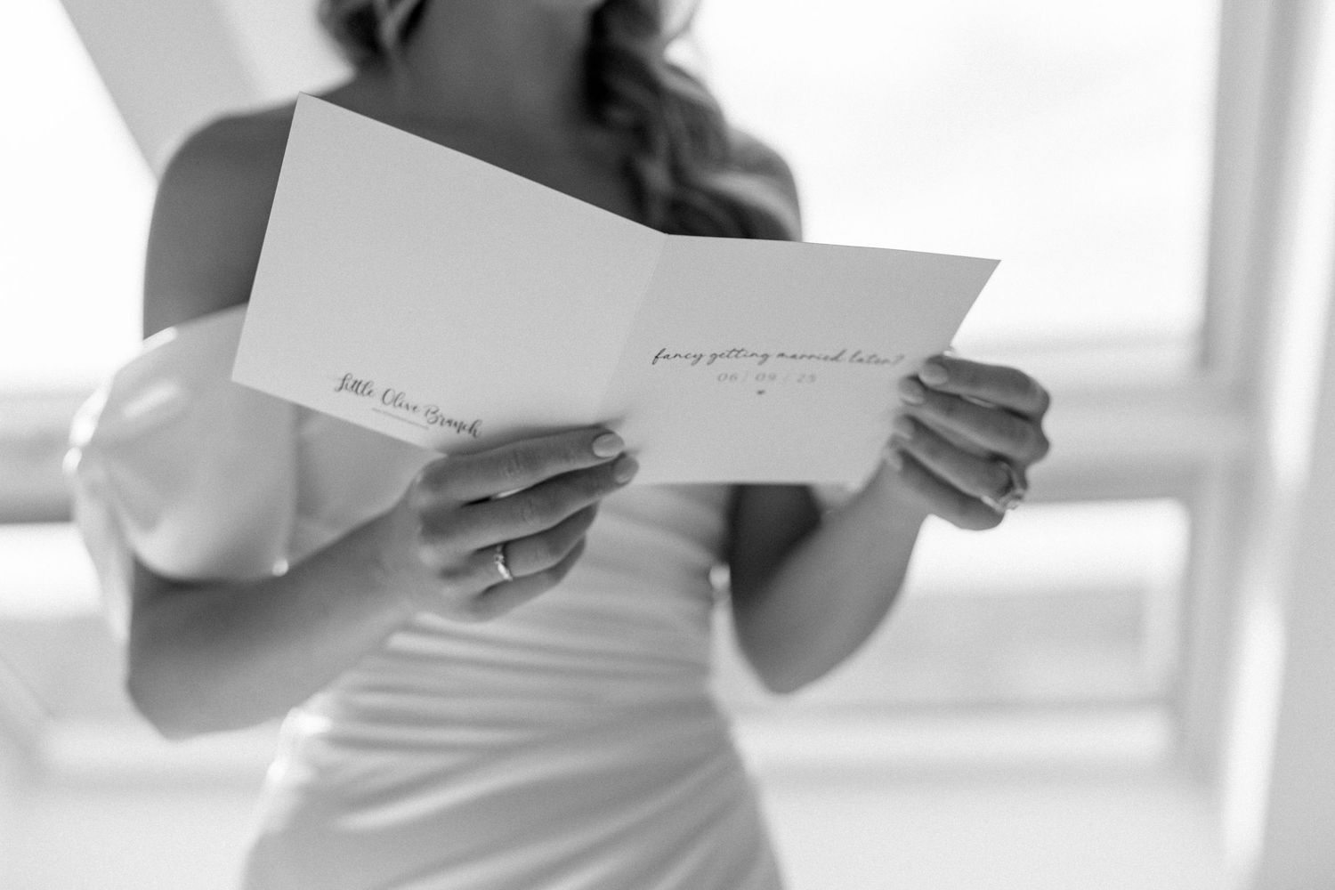 A person in a white dress reads a letter or card near a window in black and white.