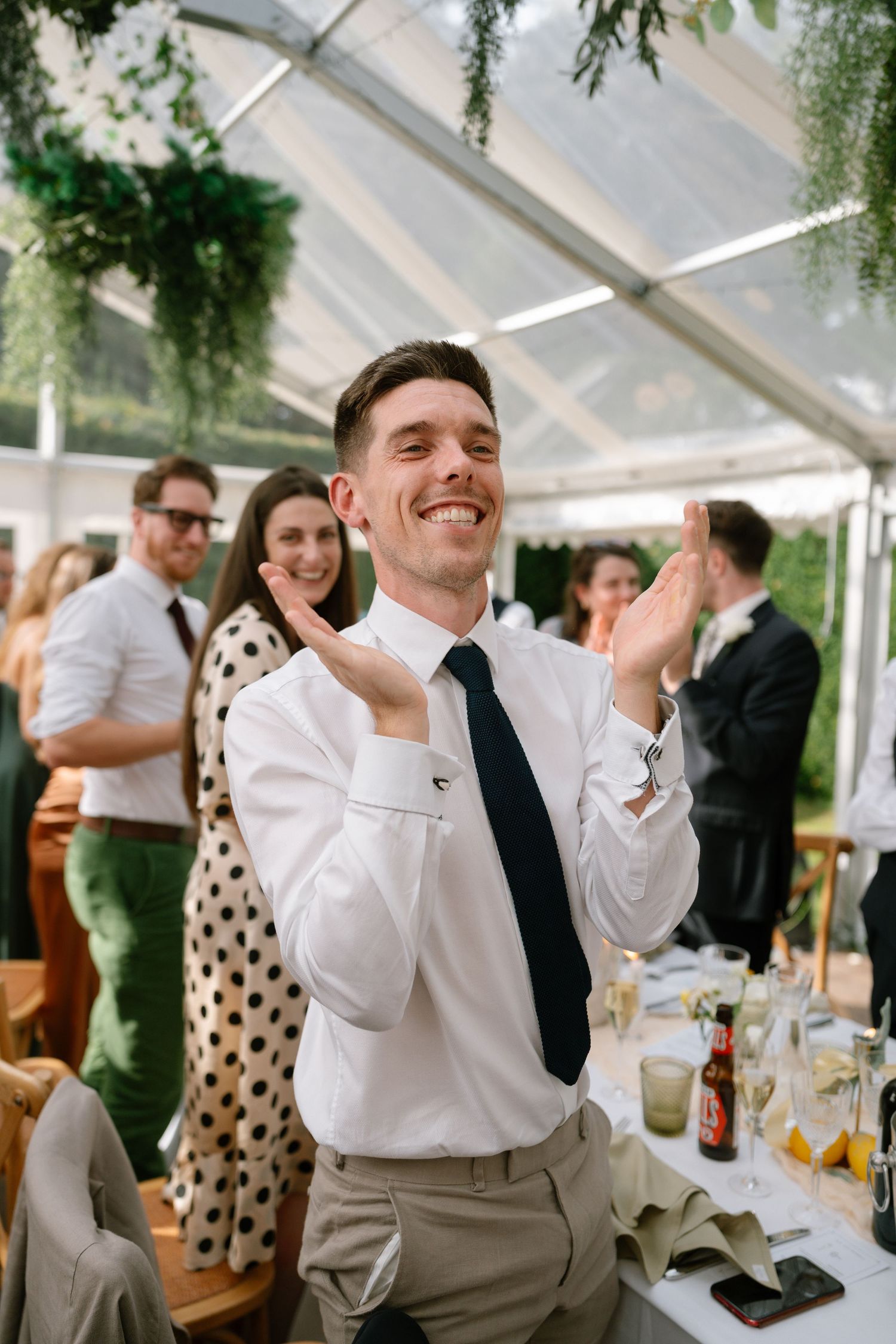 Wedding guests in formal attire sharing joyful moments under a white tent canopy.