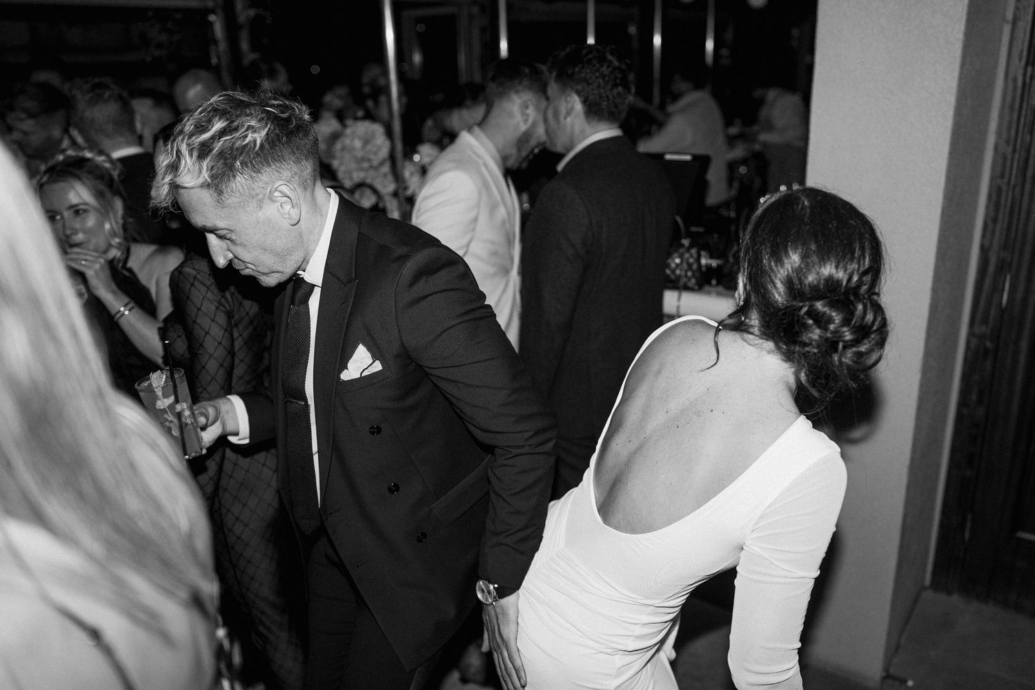 Wedding guests dance and socialize at an indoor evening reception.