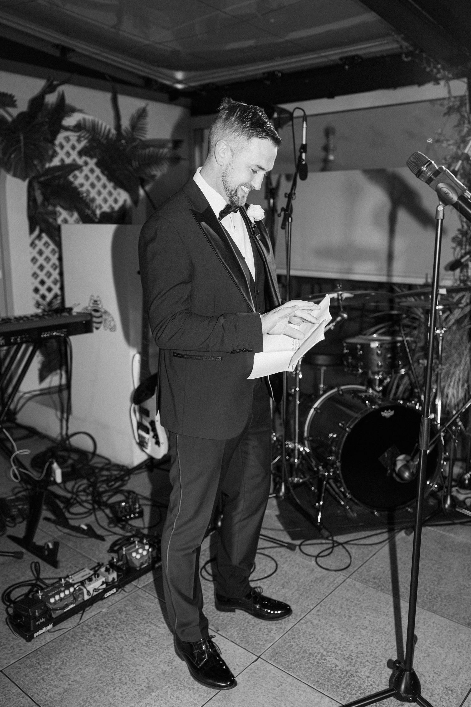 Black and white photo of speaker at wedding reception with musical equipment in background.