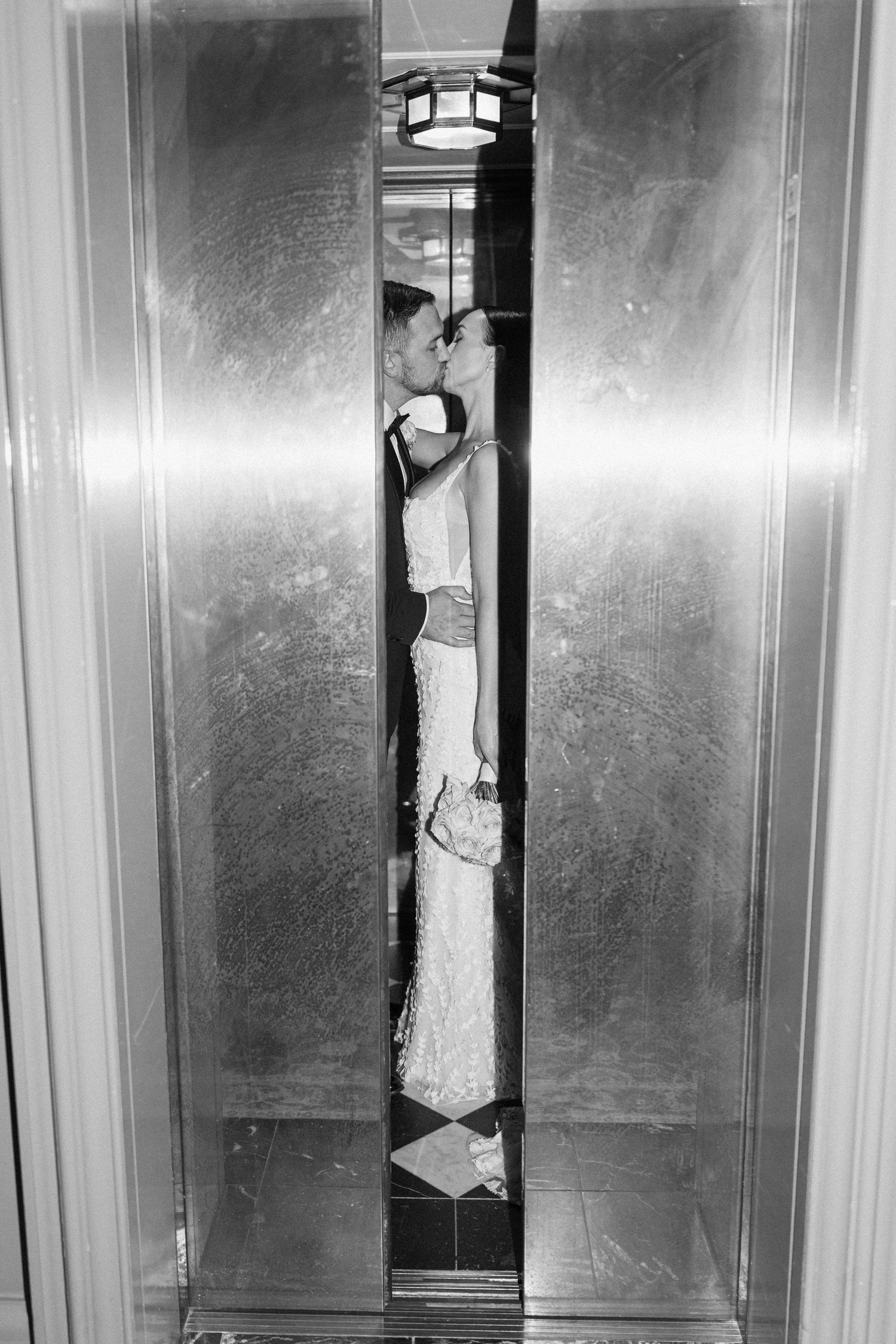 Black and white photo of newlyweds kissing in an elevator.