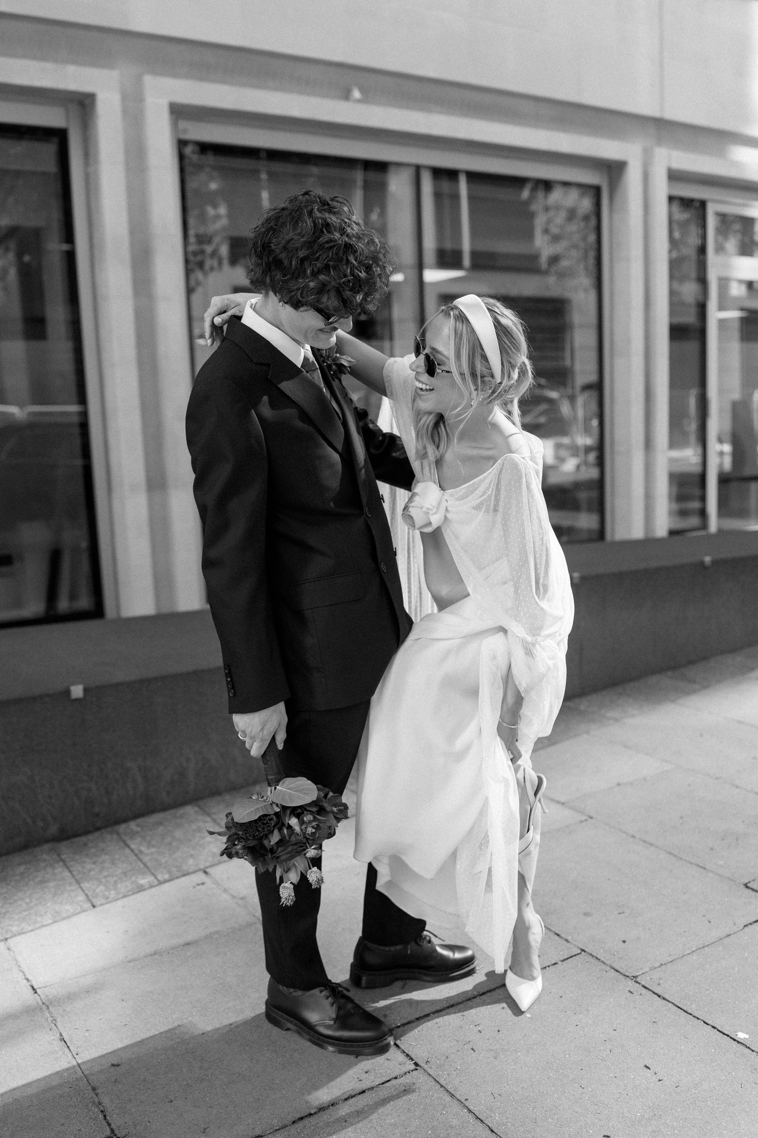Black and white photo showing wedding couple's feet as they walk along urban sidewalk.