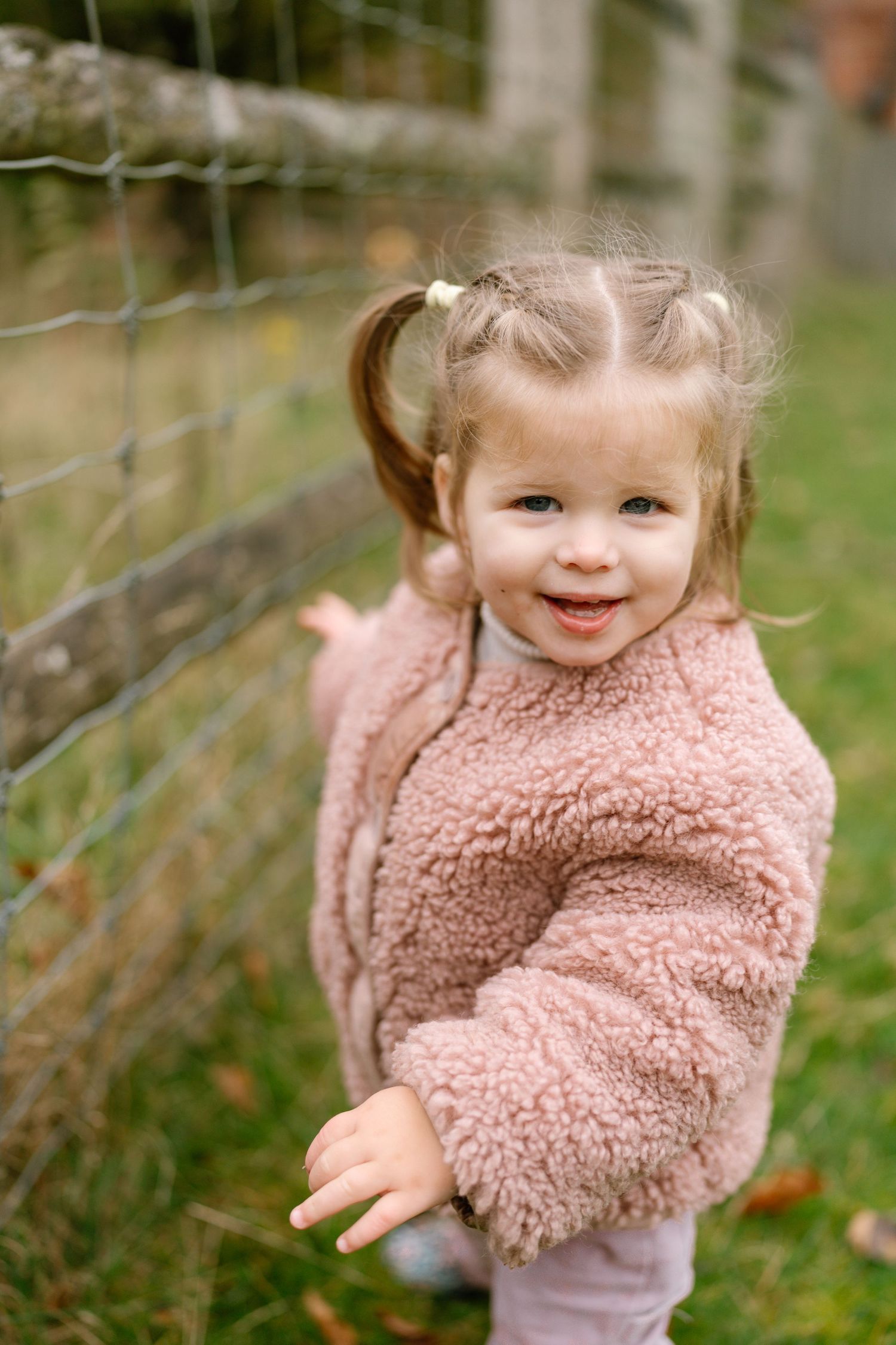 A small child in a pink fuzzy sweater plays outdoors with a joyful expression.