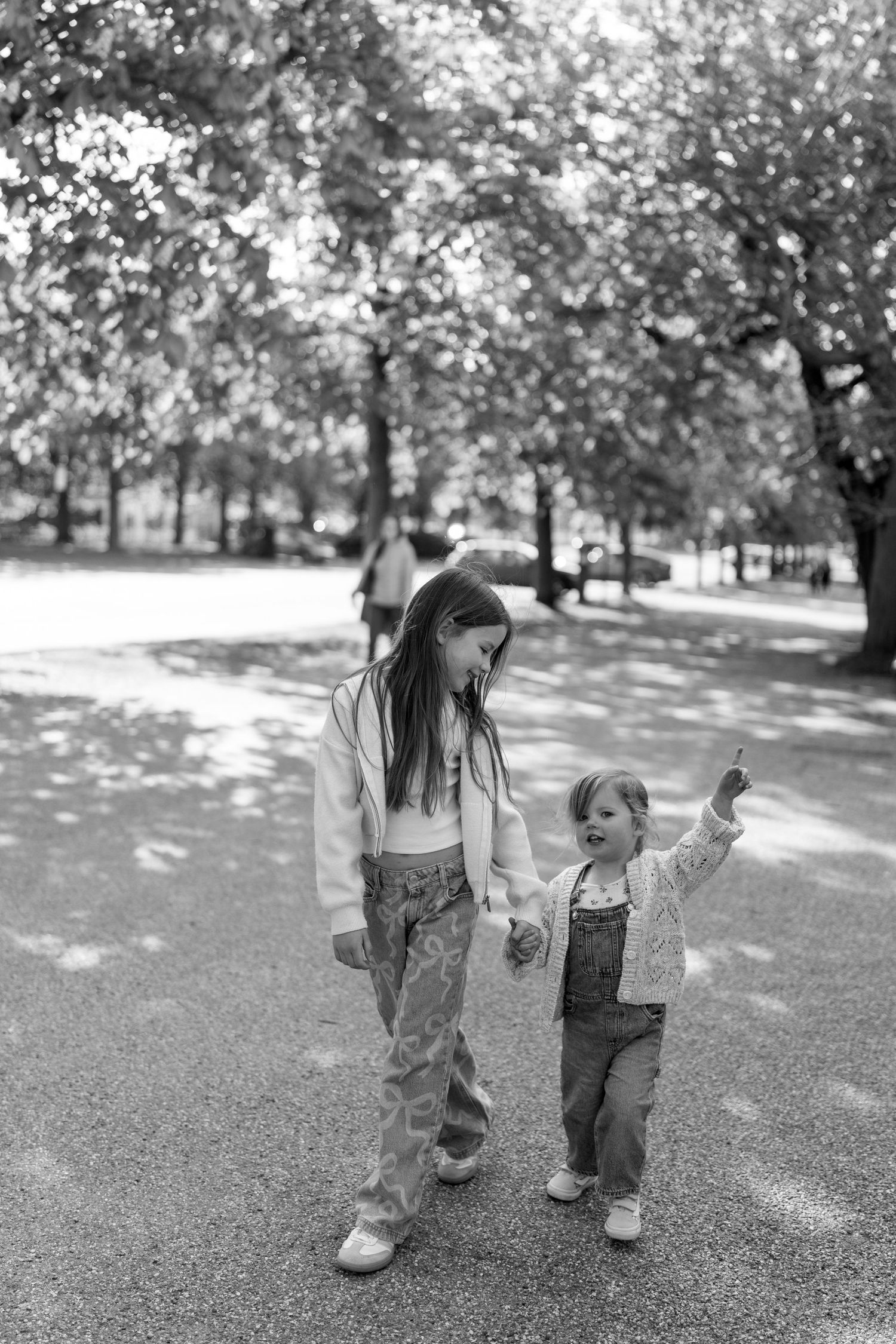 Black and white photo of two people walking together on a textured ground in dappled sunlight.