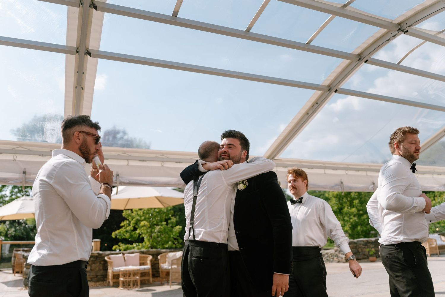 Wedding party members interacting under a white tent during daytime celebrations.