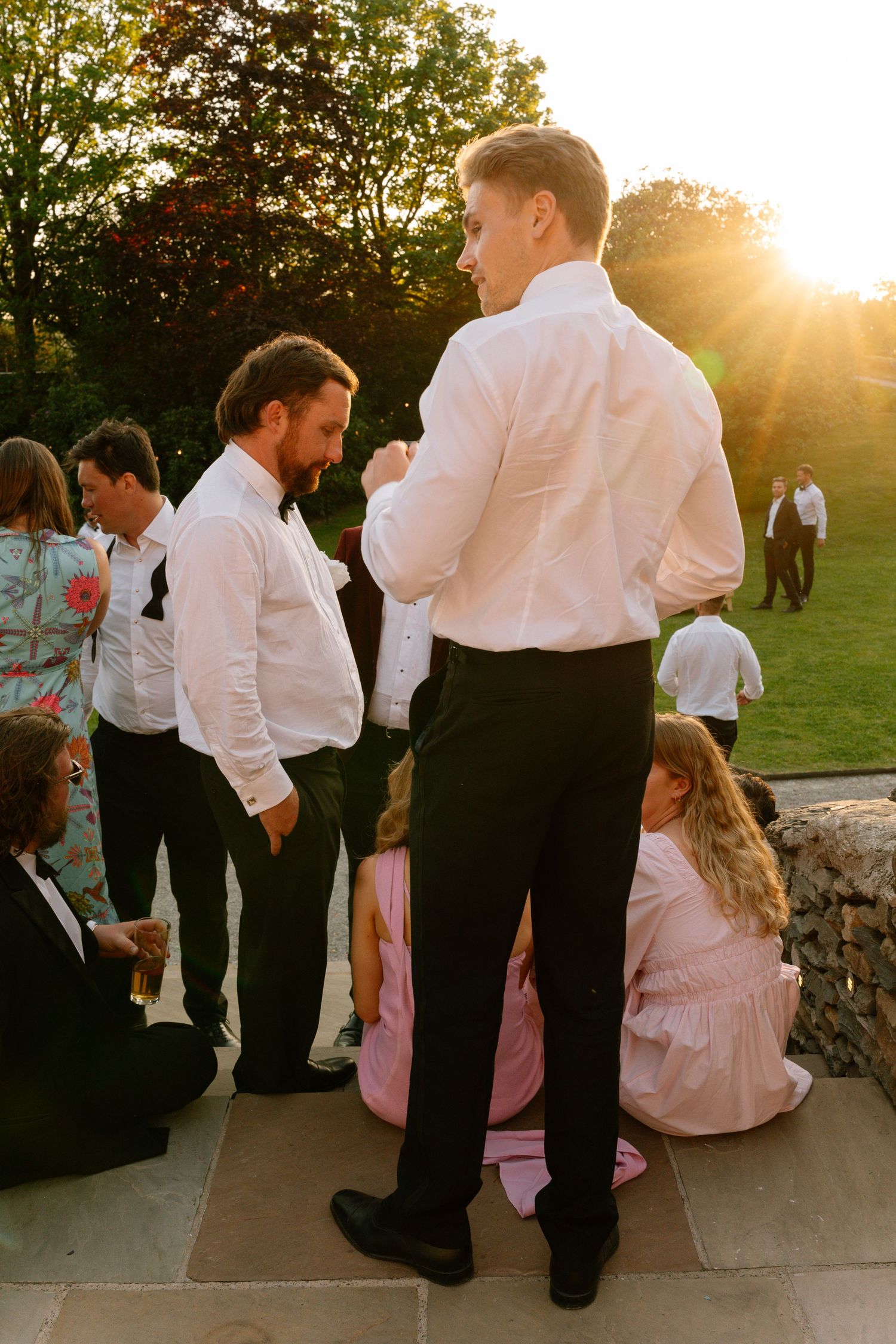 Wedding party members gather on stone steps during golden hour sunset.