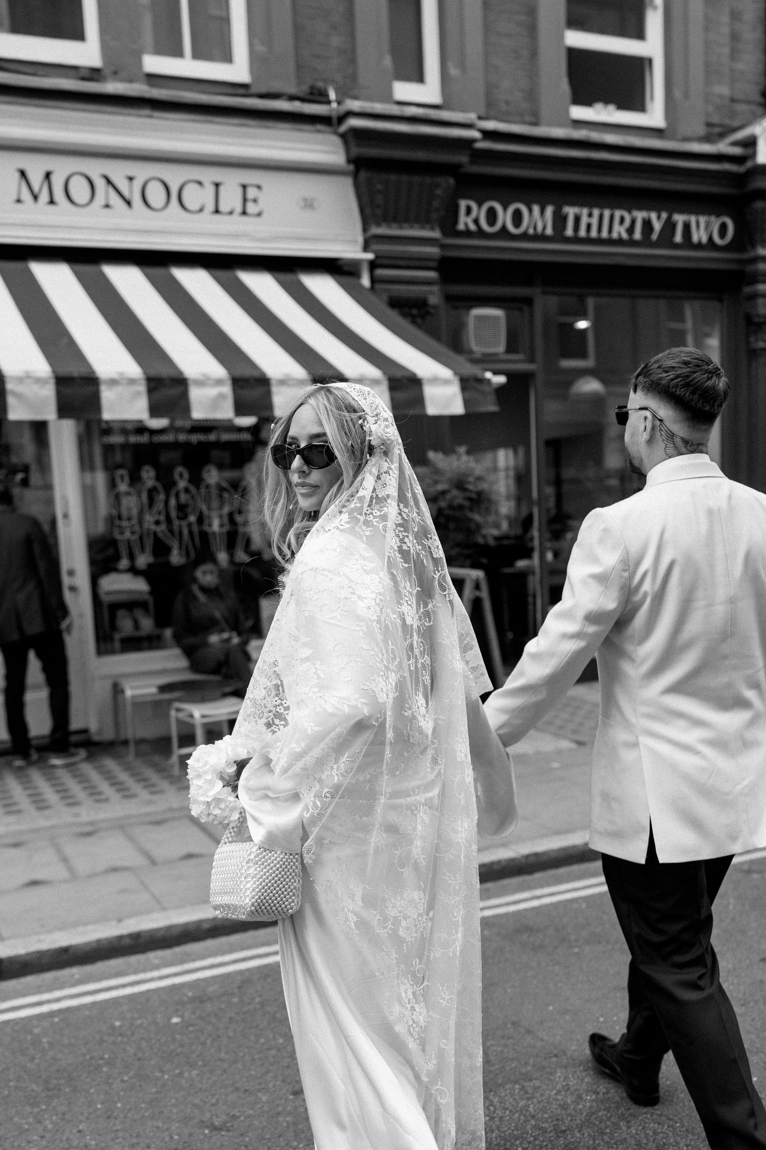 A bride and groom walk past storefronts including Monocle and Room Thirty Two.
