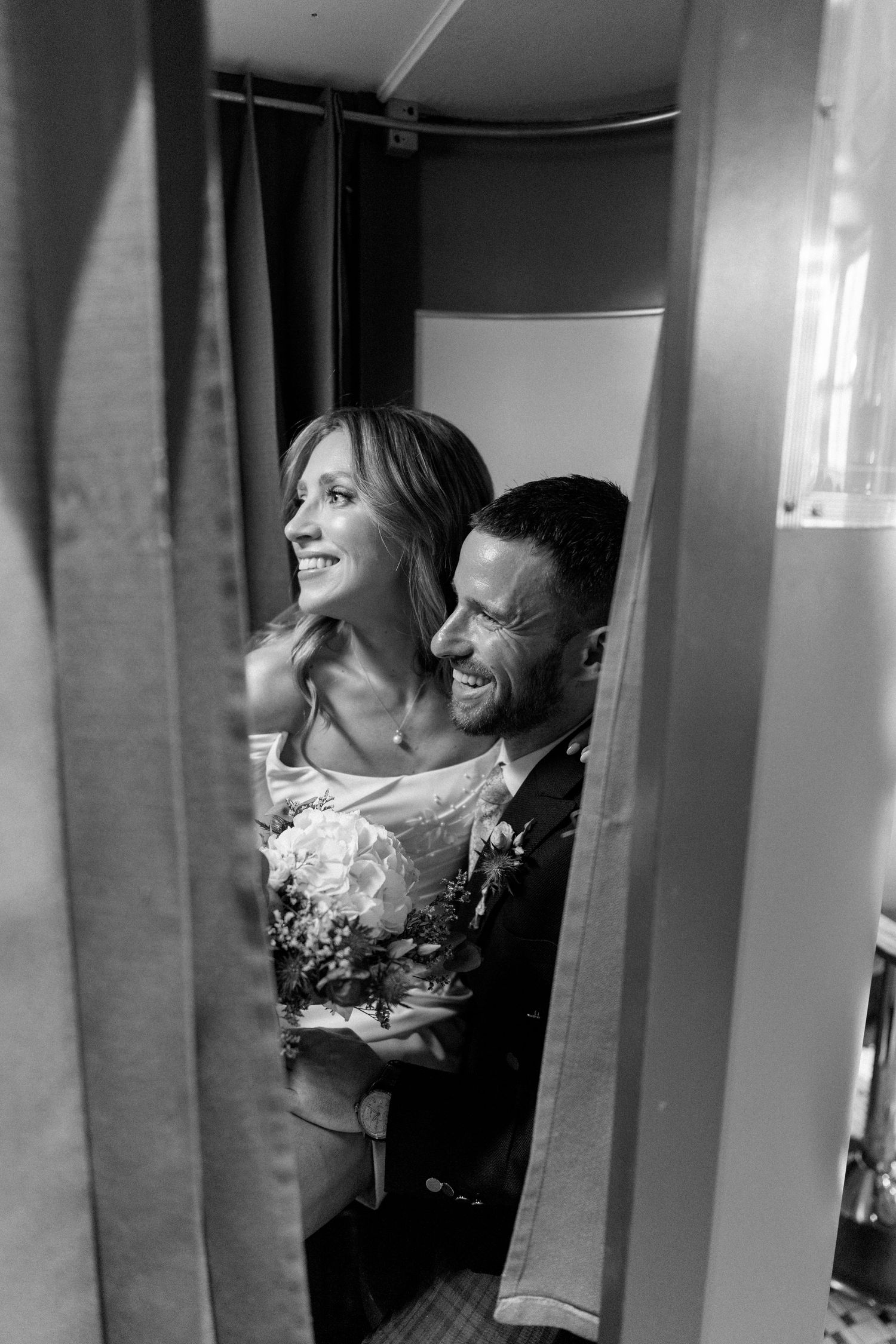 A candid black and white wedding photo showing a joyful couple laughing together behind a curtain.