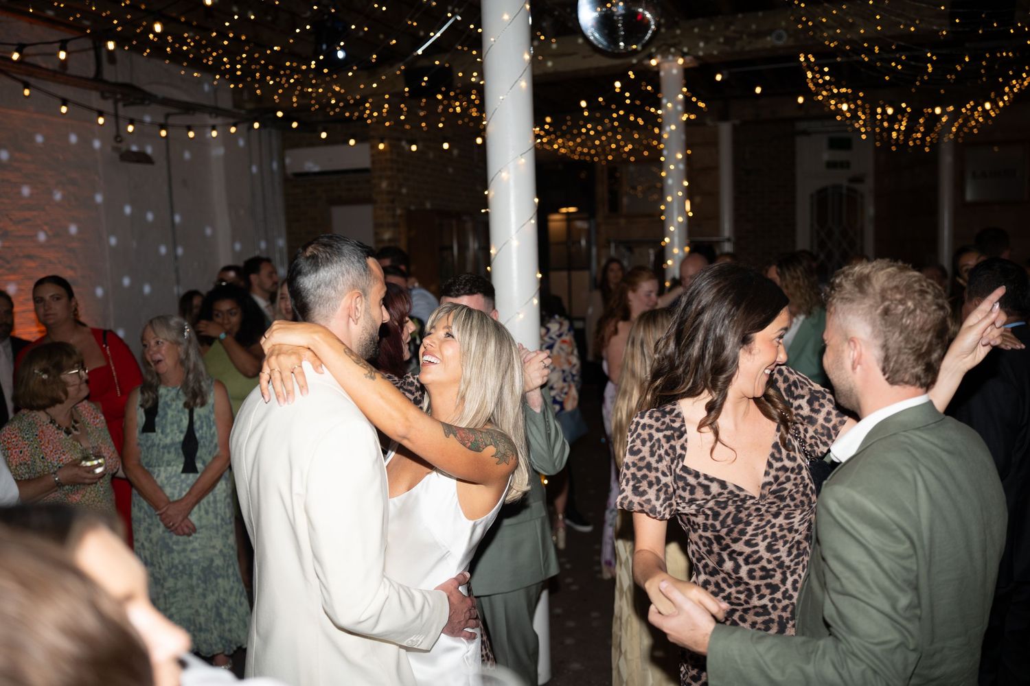 Wedding reception dance floor filled with guests under sparkling string lights.