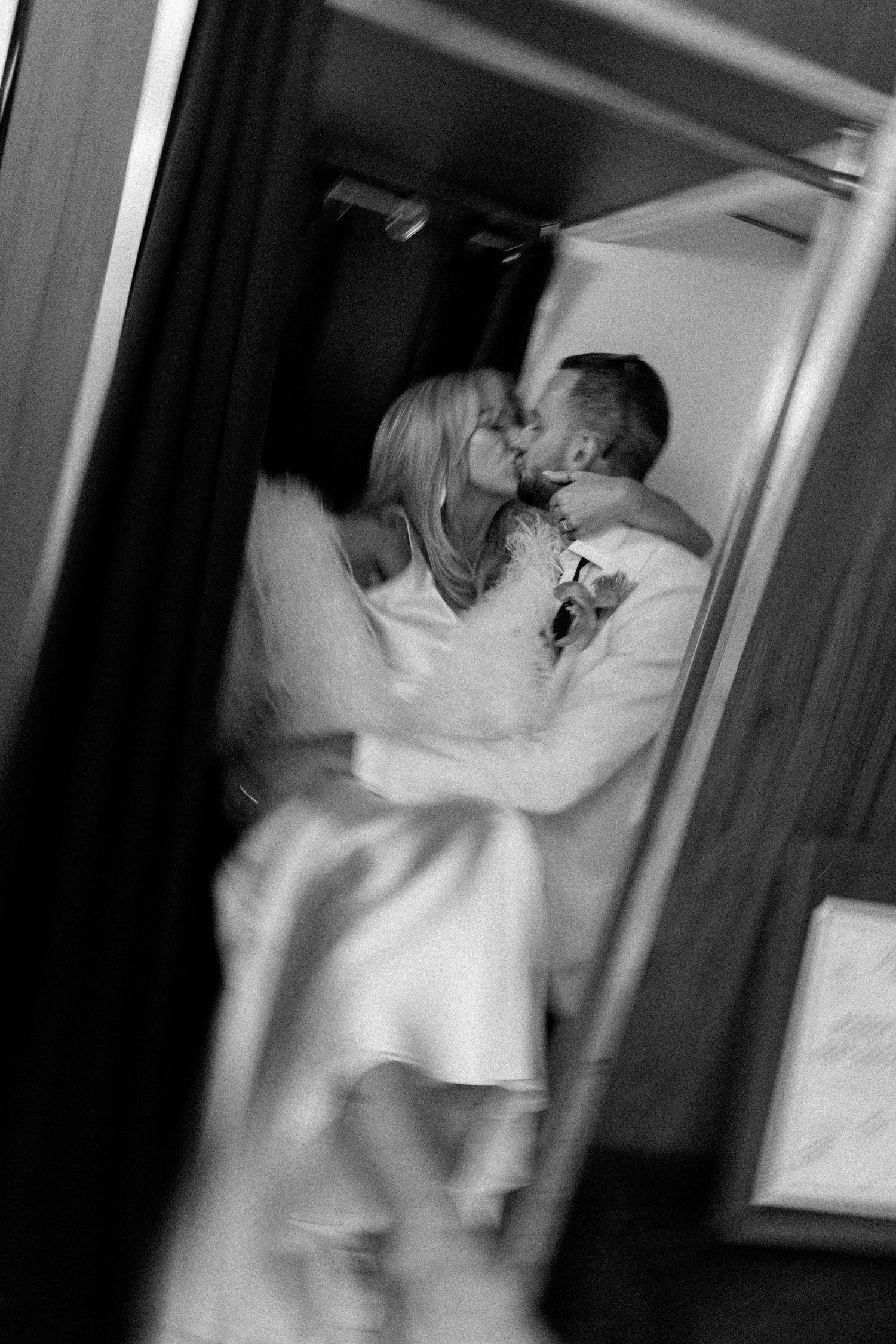 Black and white intimate moment captured through doorway of couple in wedding attire.