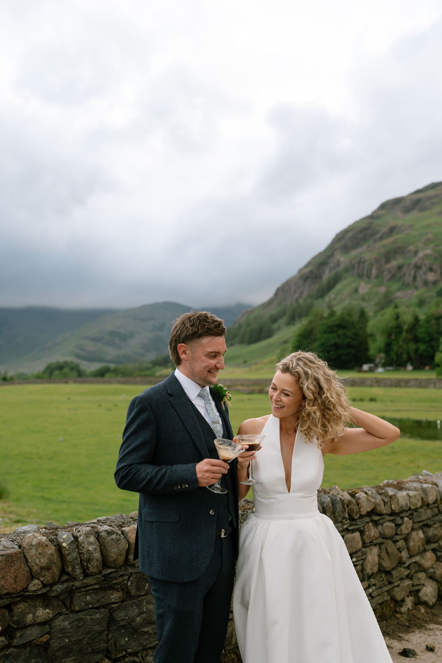 Couple sharing a moment against a backdrop of Scottish highlands and stone wall.