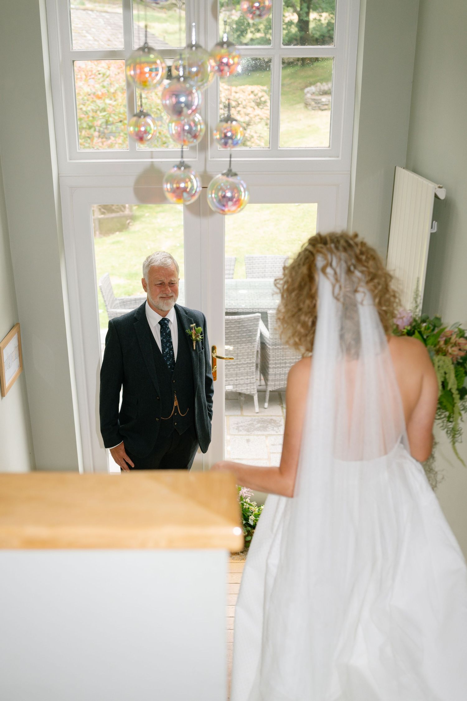 Emotional first look moment between bride and father in sunlit room.
