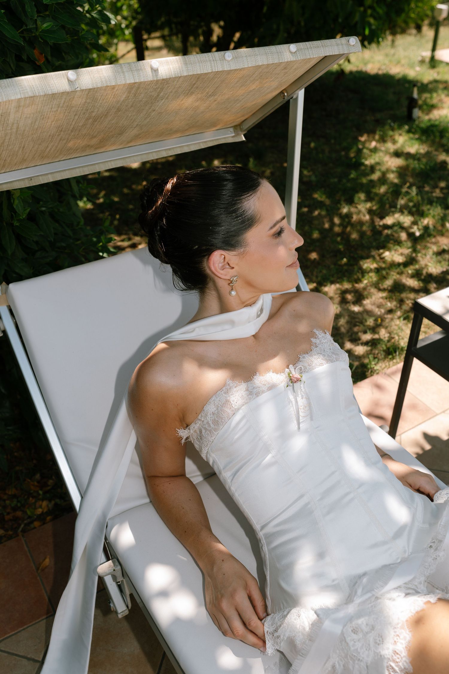 Person in white dress reclining on outdoor lounge chair under dappled sunlight.