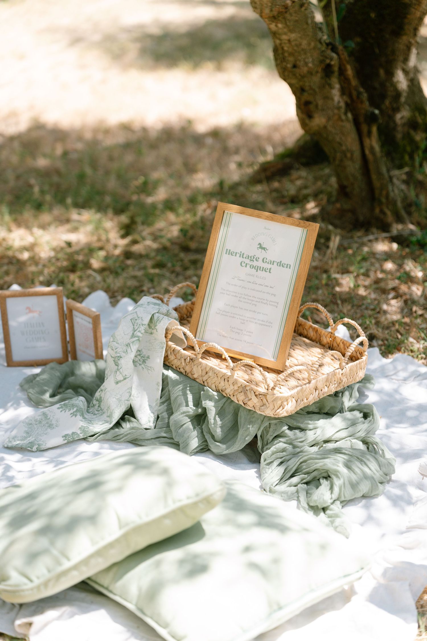 Framed wedding signage displayed on white fabric with delicate sage green accents in an outdoor setting.
