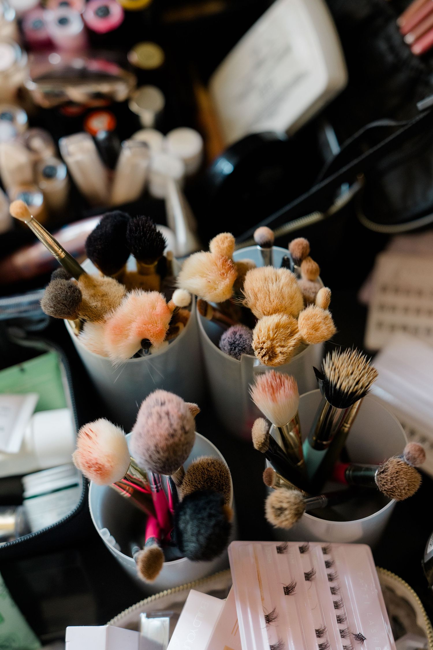 Collection of professional makeup brushes in white holders with false lashes on a busy bridal makeup artist table.